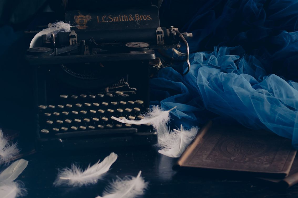 A vintage typewriter with scattered white feathers and blue fabric creating a dreamy, artistic composition.