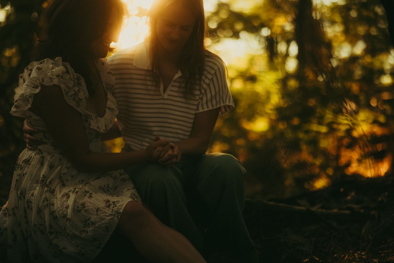 Silhouetted figures embrace in a romantic sunset with golden light filtering through trees in the background.