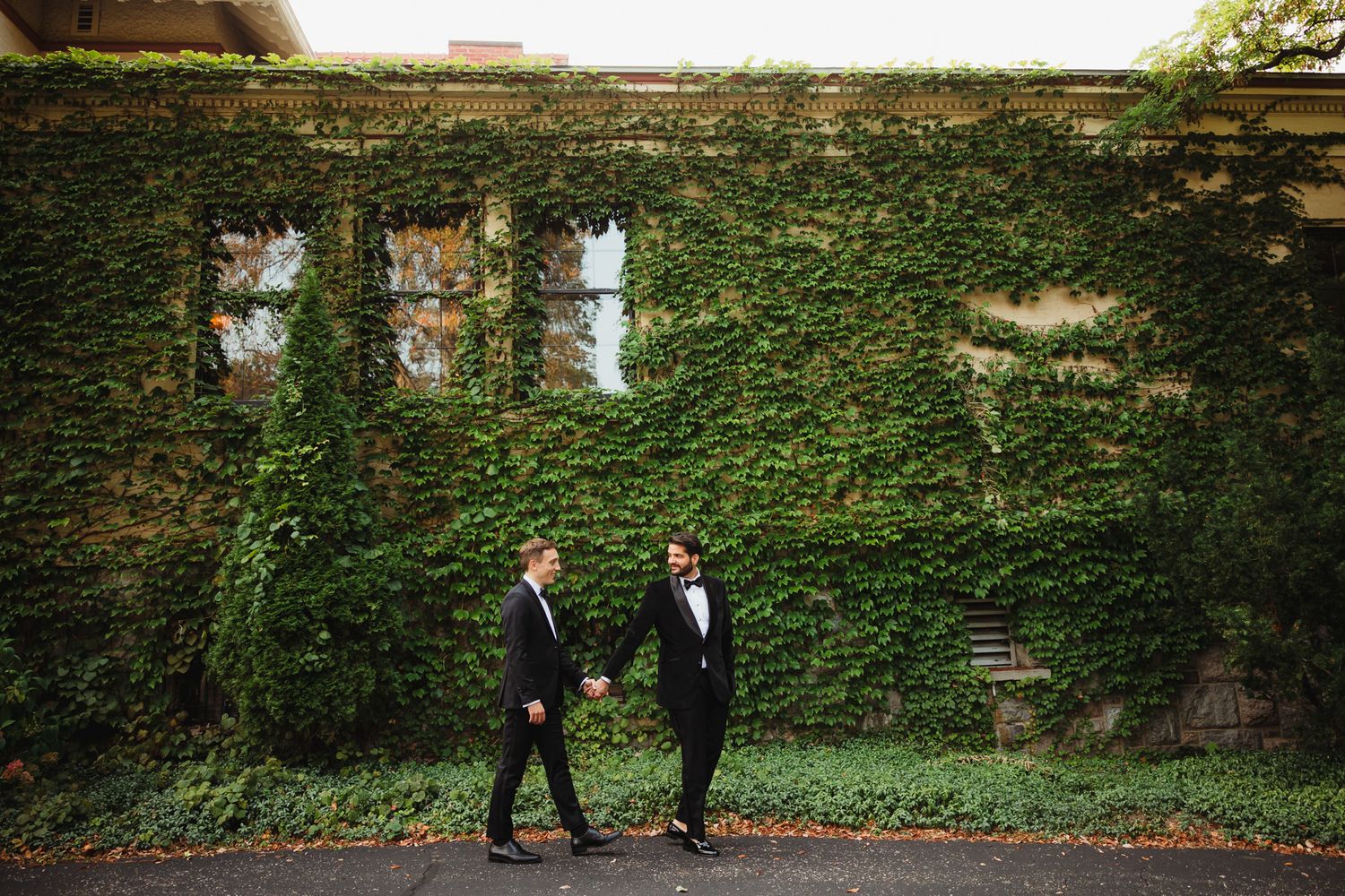 Two people walk along an ivy-covered wall in a romantic garden setting.