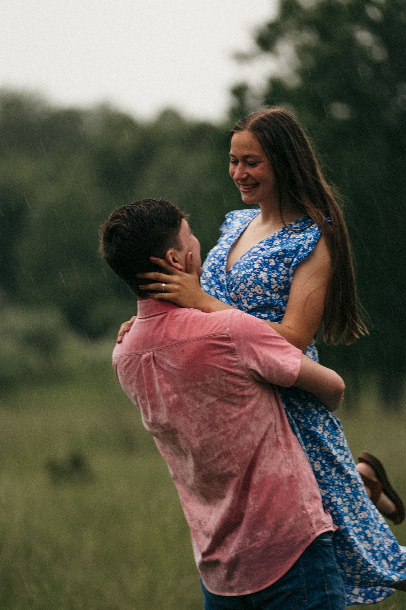Couple embracing in a field wearing blue dress and pink shirt.