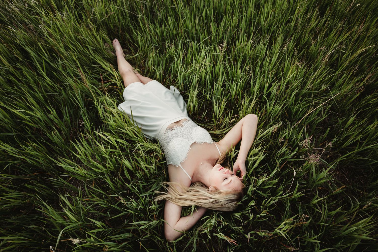 Figure in white dress lying in tall green grass field during summer.