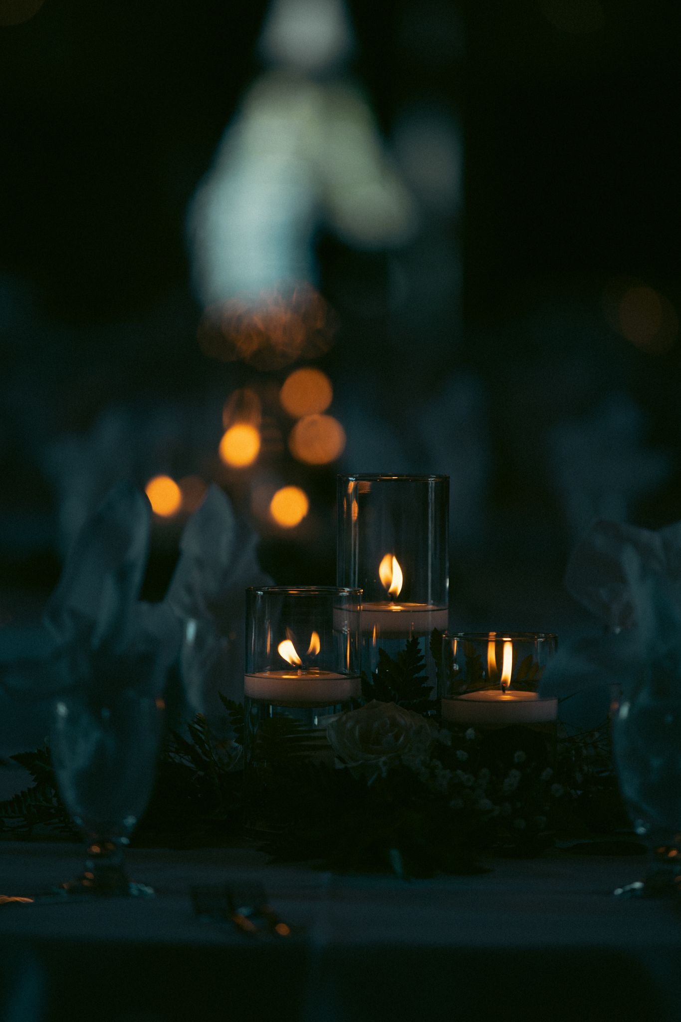 Glowing candles in glass holders create a cozy atmosphere against a dark background with soft bokeh lighting effects.