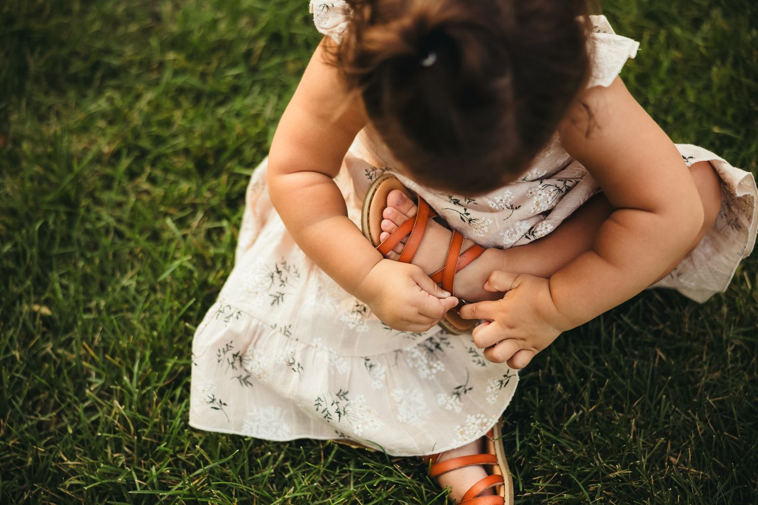 Close-up details of brown leather sandals and white dress on grassy background in natural lighting.