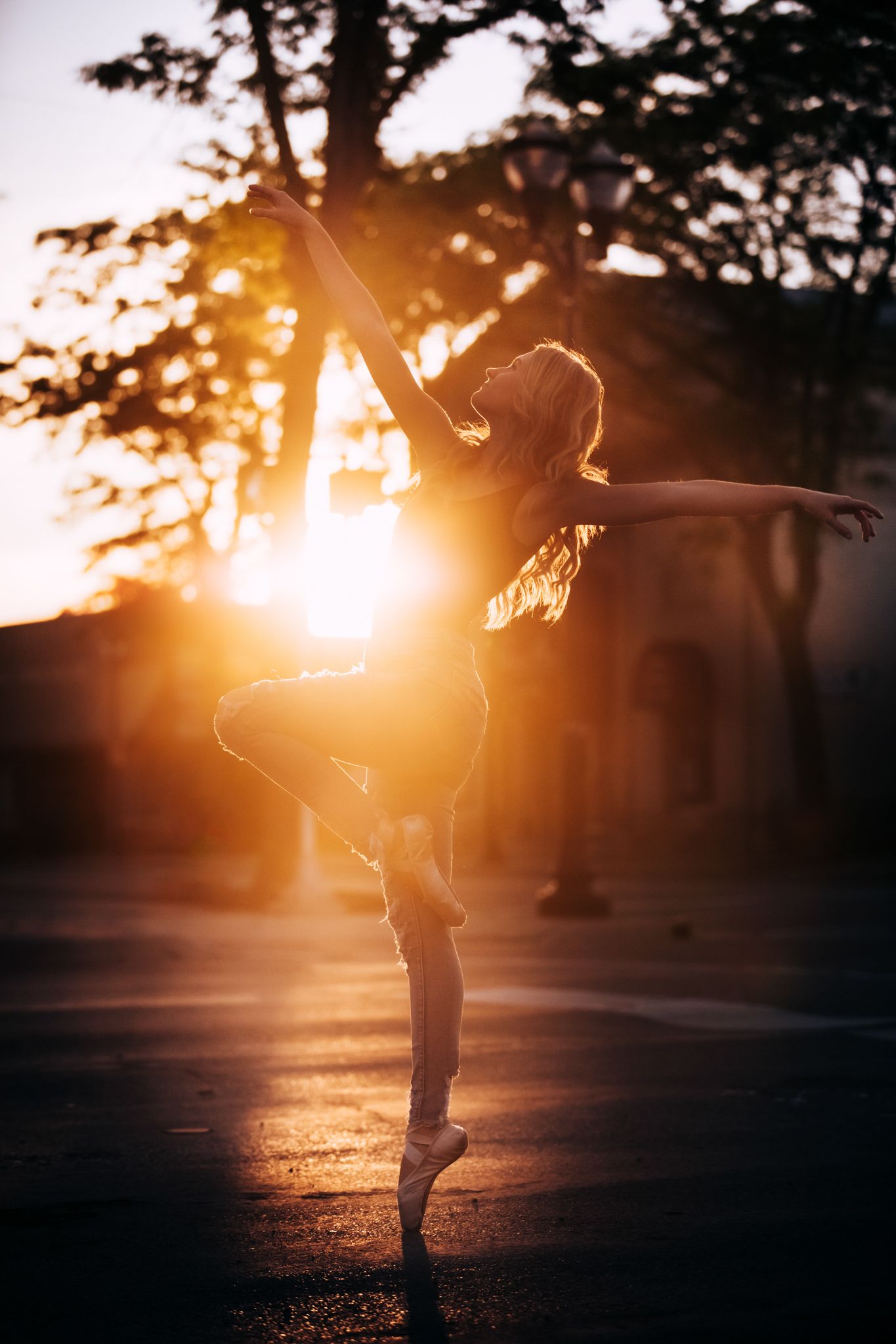 Silhouette of a ballet dancer in graceful pose against golden sunset through trees.