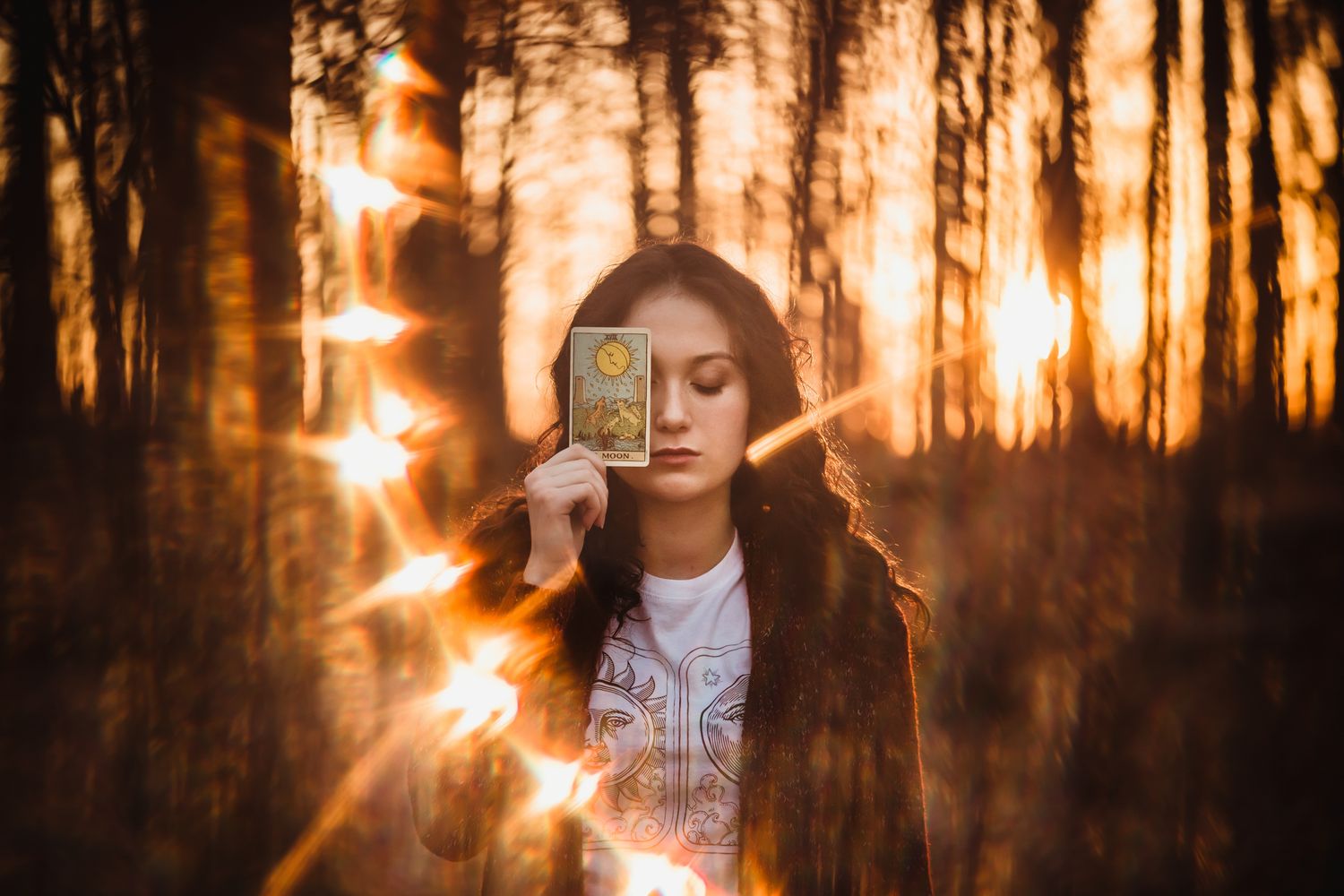 A person stands silhouetted in a golden sunlit forest with sun flares creating a dreamy atmosphere.