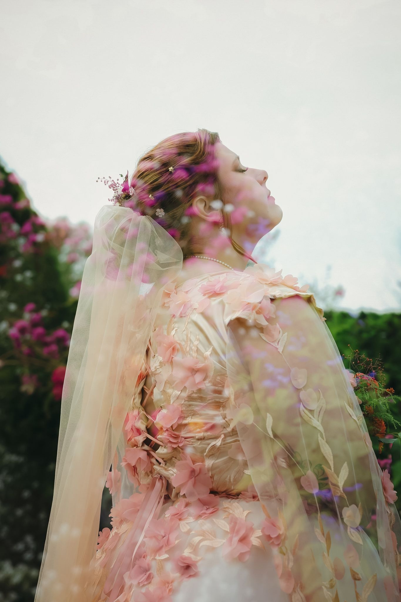Dreamy double exposure portrait through delicate pink flowers and sheer fabric.