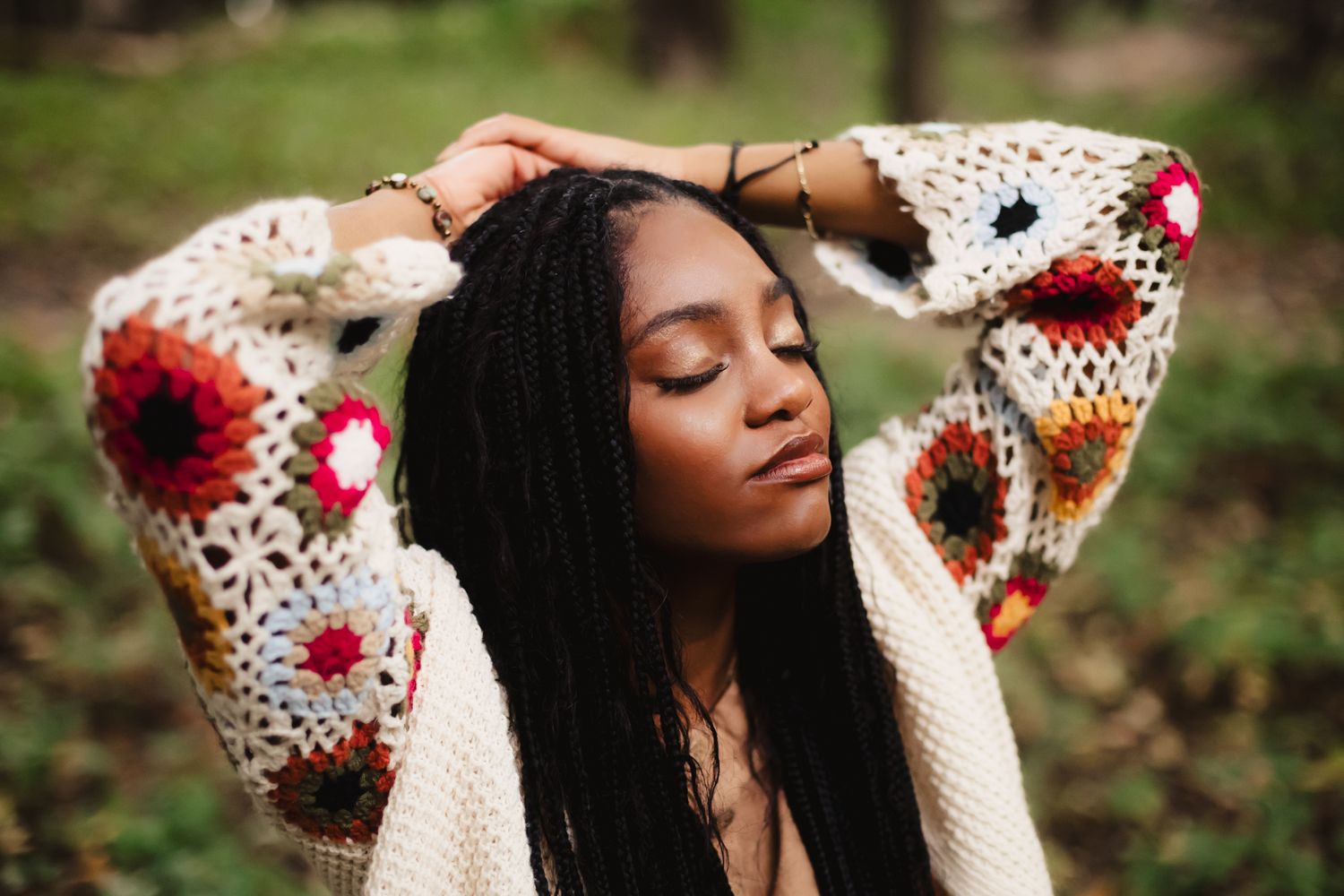 Person wearing patterned sweater with red and white details poses outdoors in natural setting.