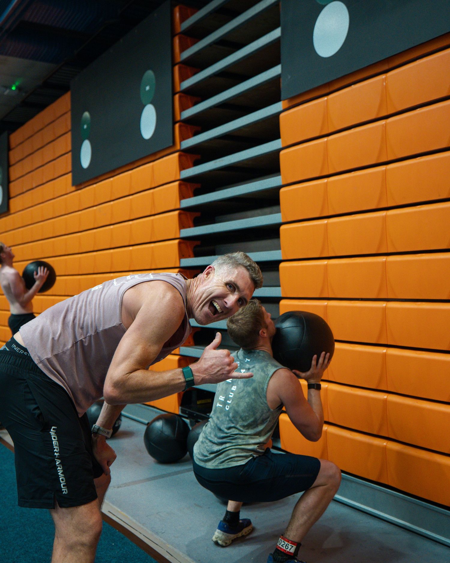 Fitness enthusiast performing dumbbell exercises with proper form against orange gym wall panels.