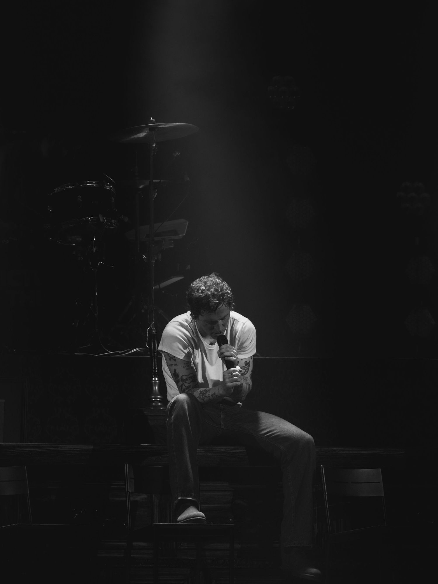 Dramatic low-key portrait of seated performer in spotlight on dark stage.