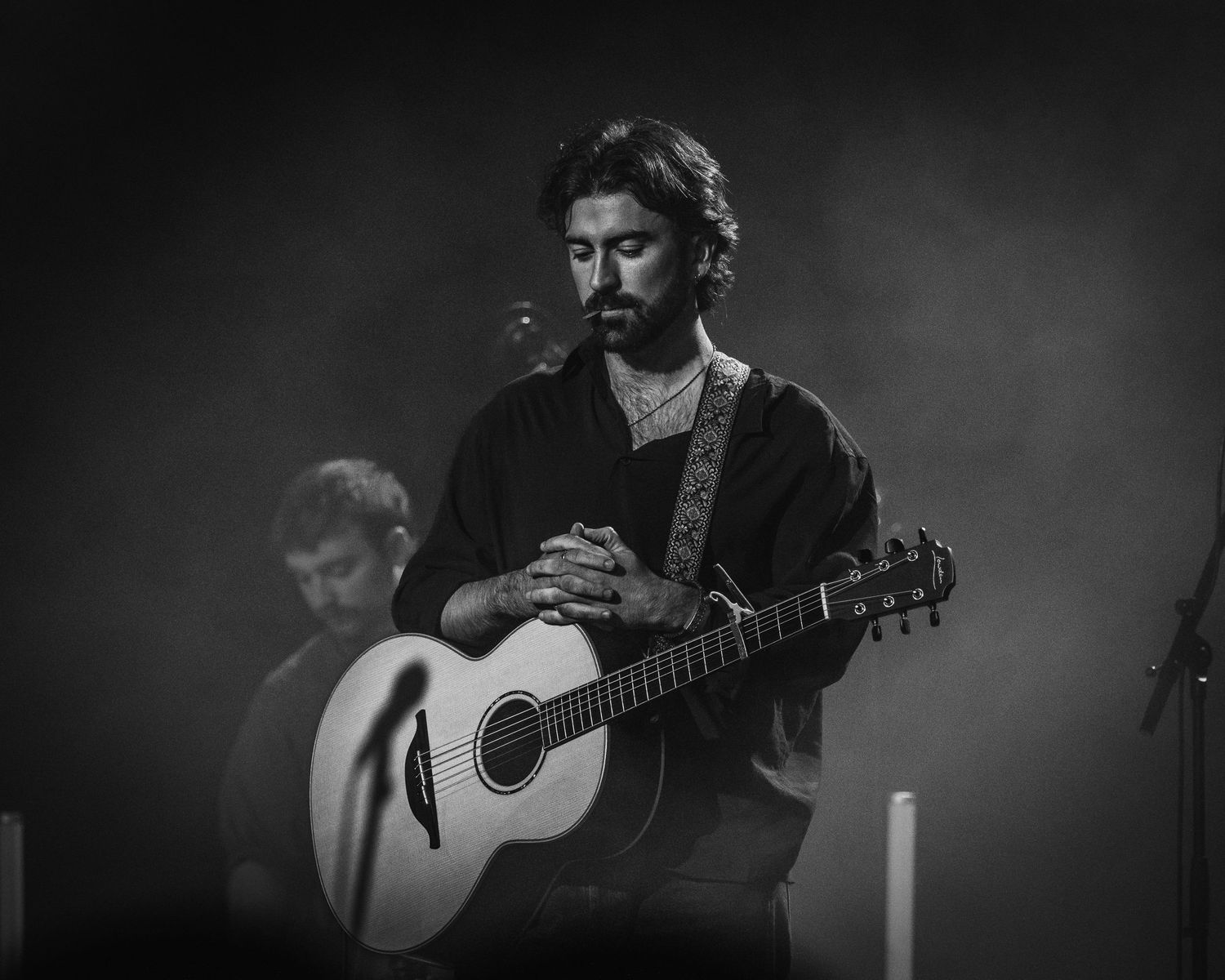 A dramatic black and white photo of a musician playing acoustic guitar on stage in moody lighting.