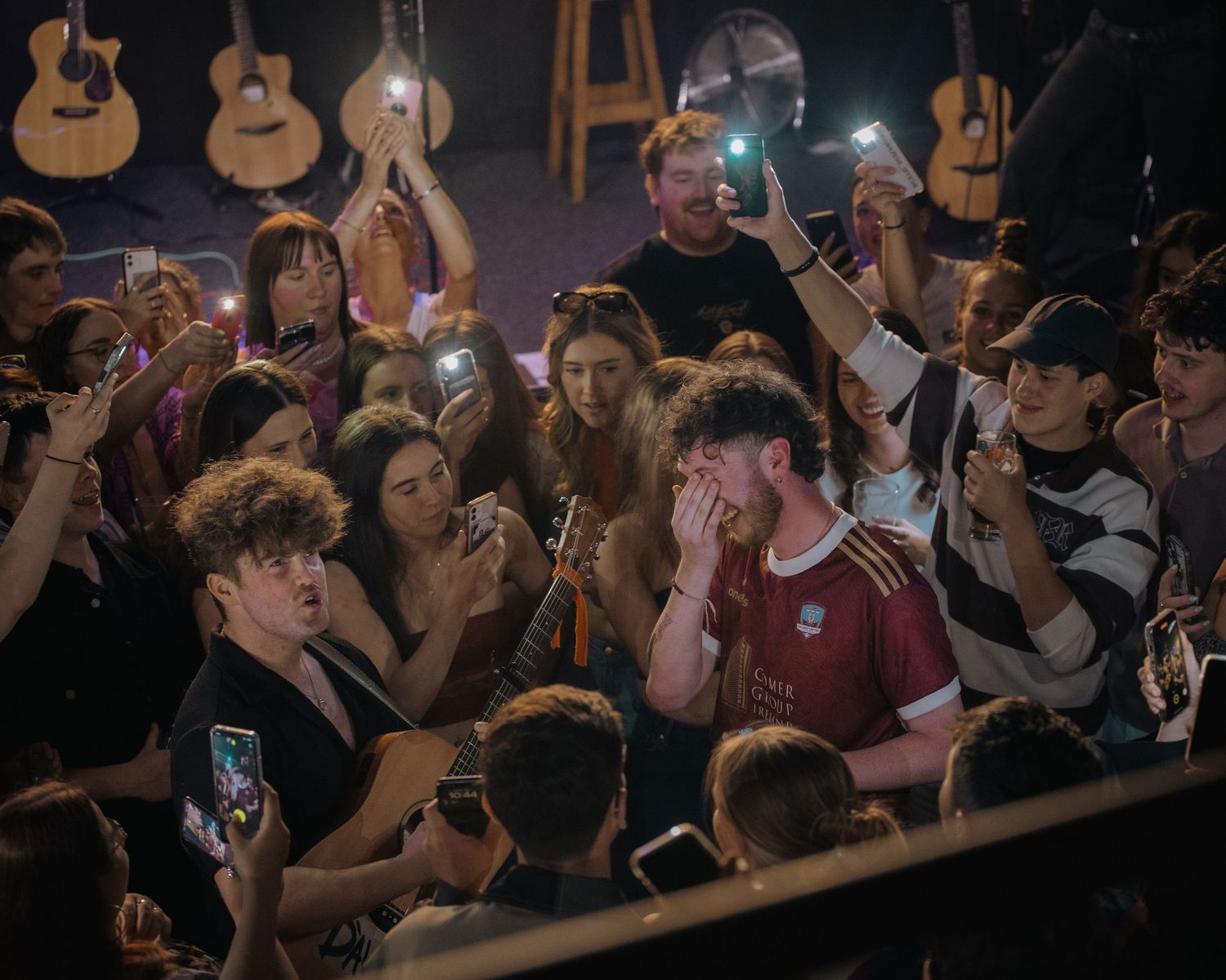 Enthusiastic concert crowd reaching towards the stage with phones raised to capture the moment.