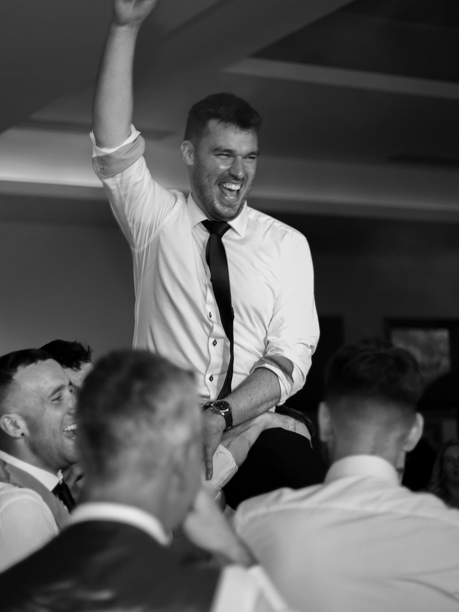 Black and white photo of wedding reception guests dancing and celebrating with raised arms.
