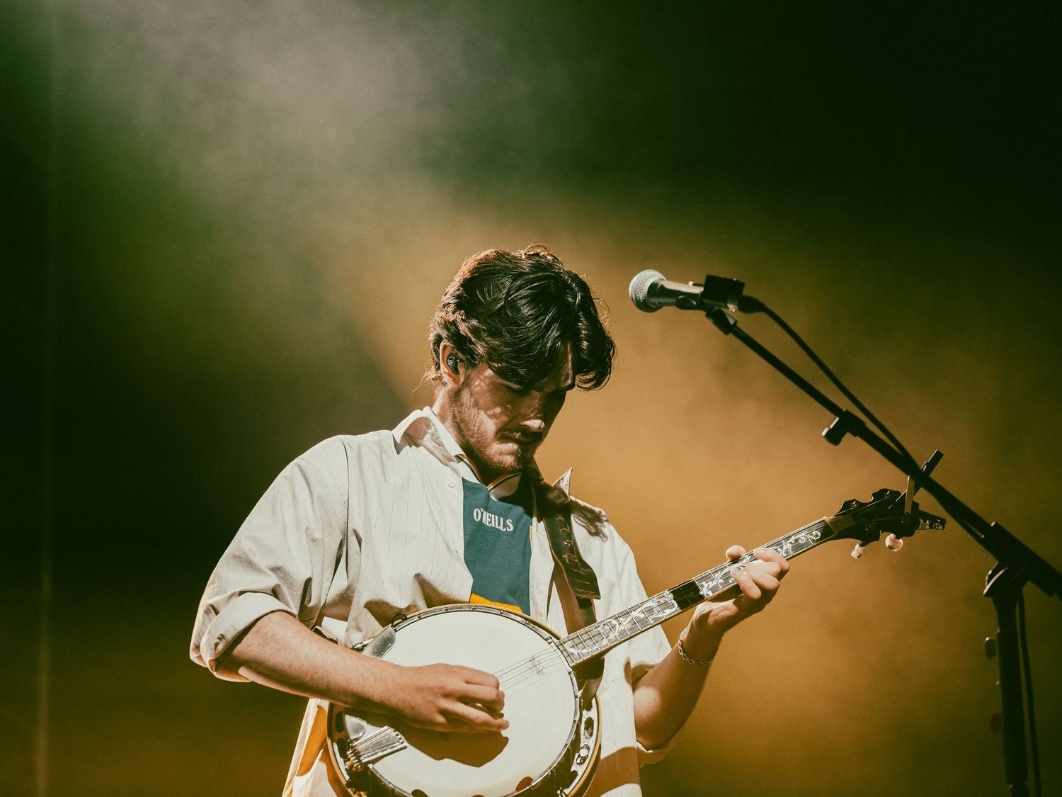 A guitarist performs on stage with dramatic lighting and a warm brown background.