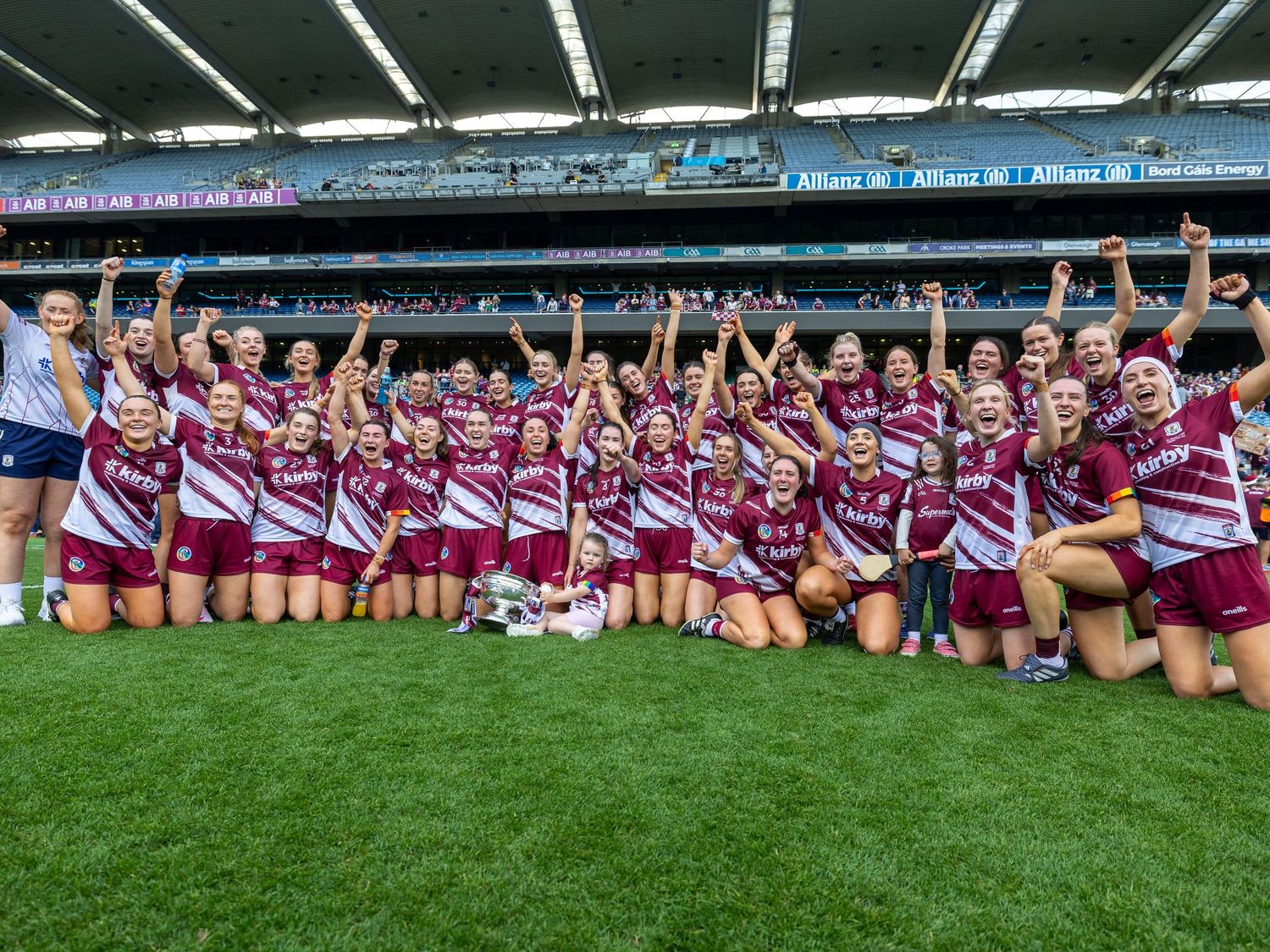 Sports team in maroon and white striped jerseys celebrates together on field after victory at stadium.