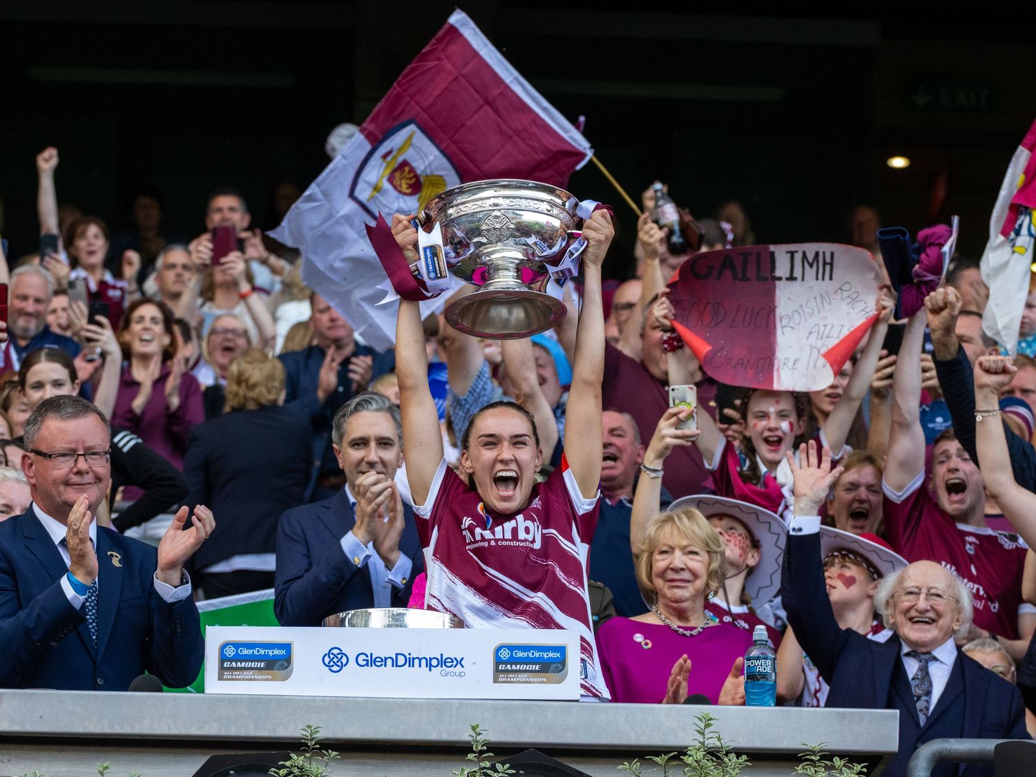 Sports team celebrating with trophy while crowd cheers in stadium stands.