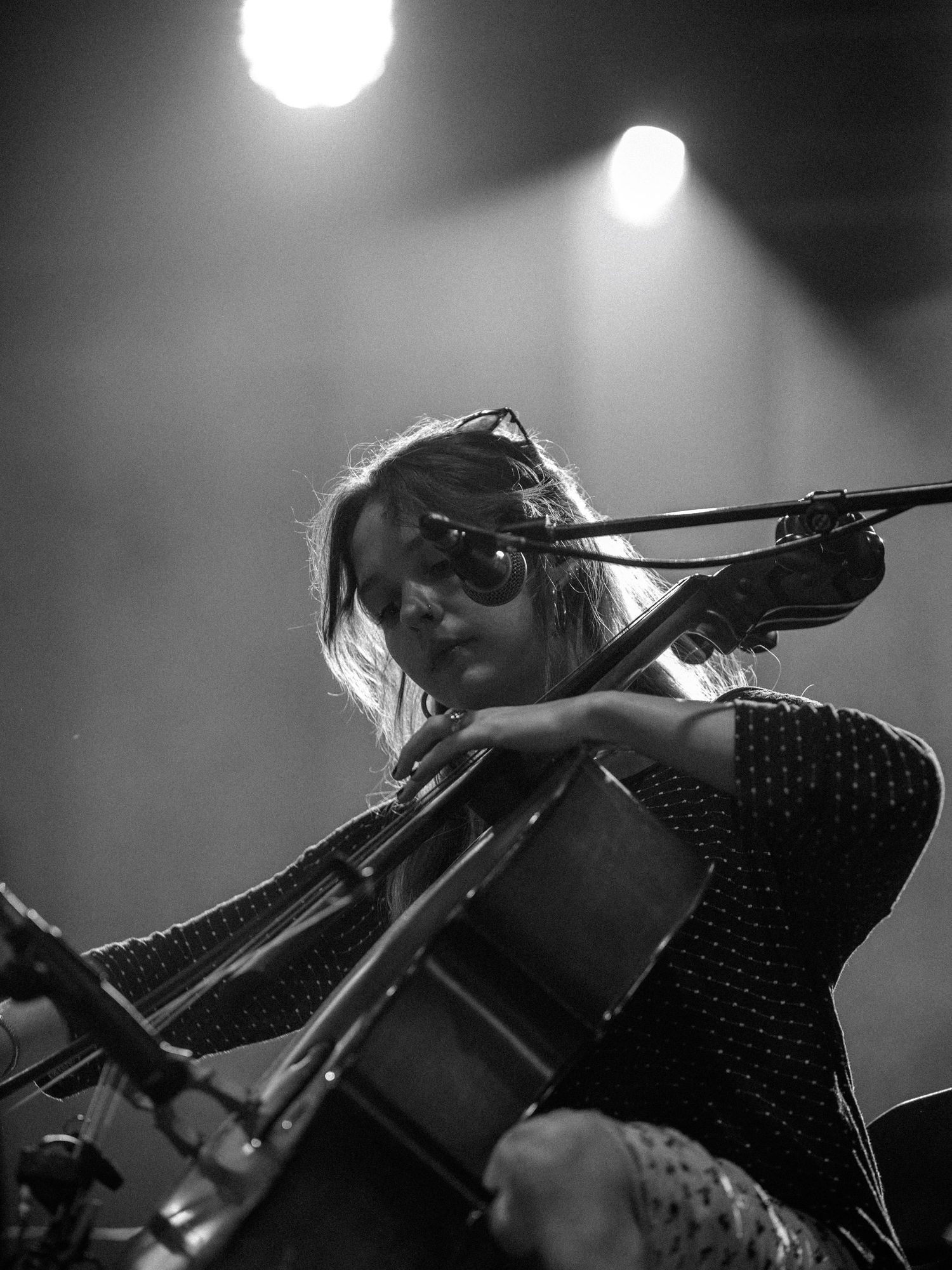 Musician plays cello on dimly lit stage with spotlights creating atmospheric ambiance.