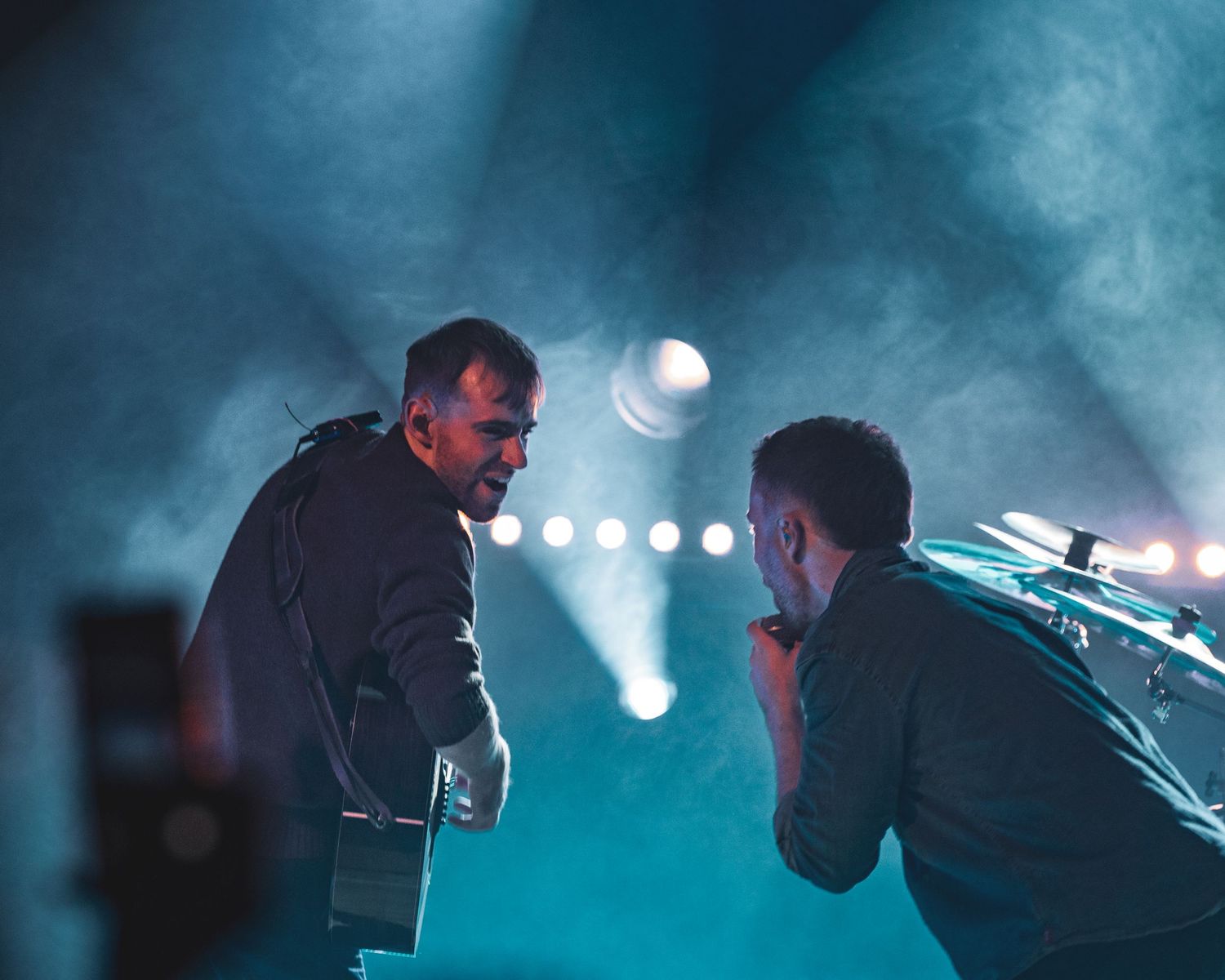 Musicians performing on a misty stage with ethereal teal lighting creating a moody atmosphere.