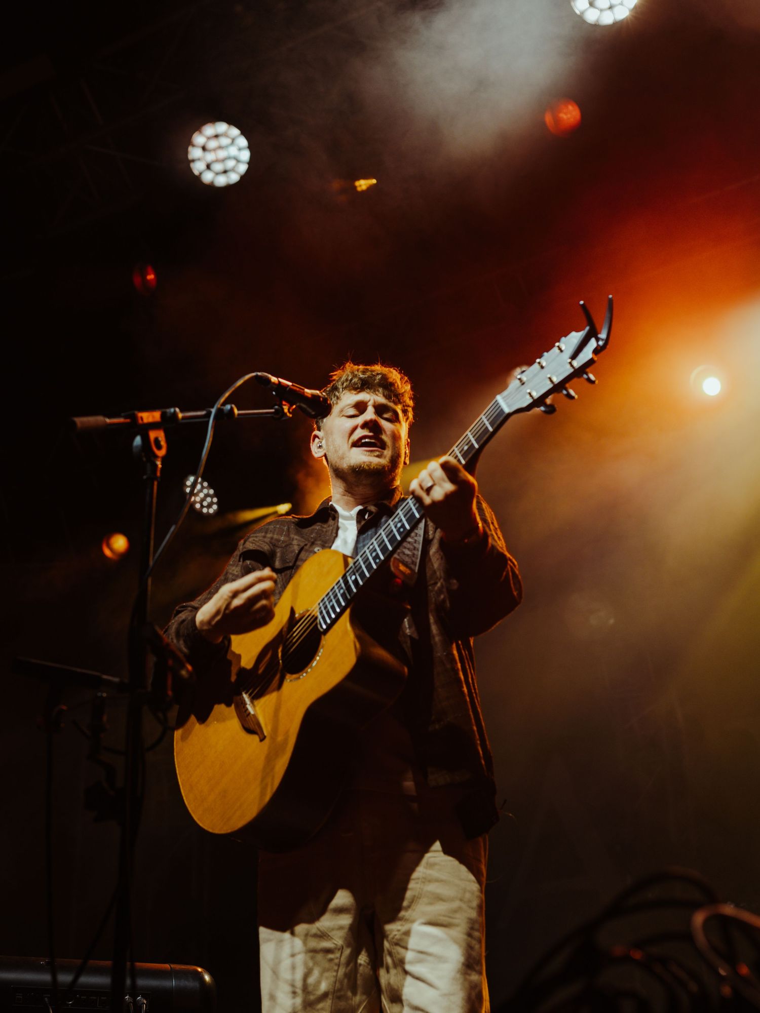 Musician plays acoustic guitar under warm red stage lighting with disco ball overhead.