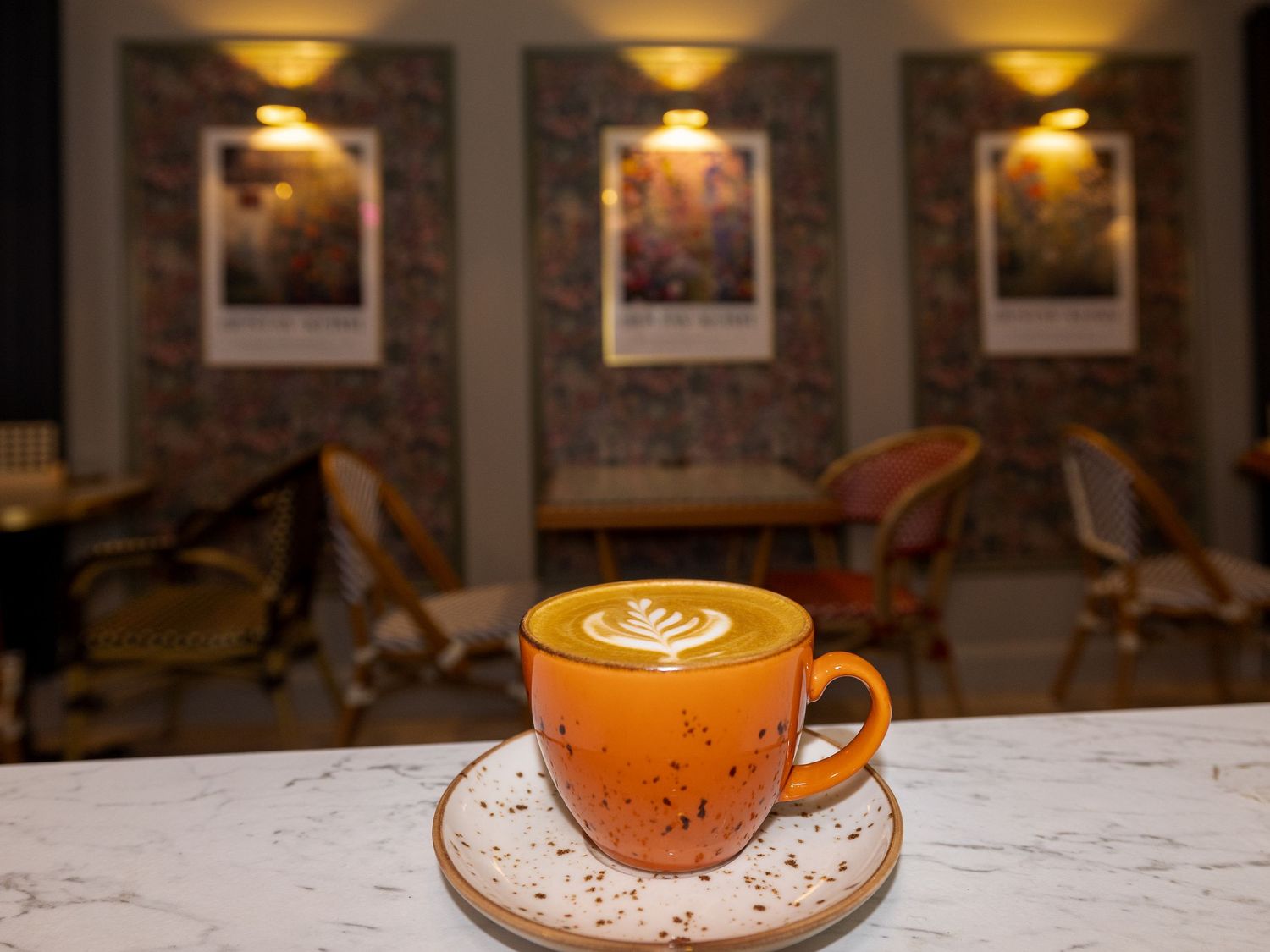 Orange coffee cup with latte art on white marble table in cozy cafe interior.