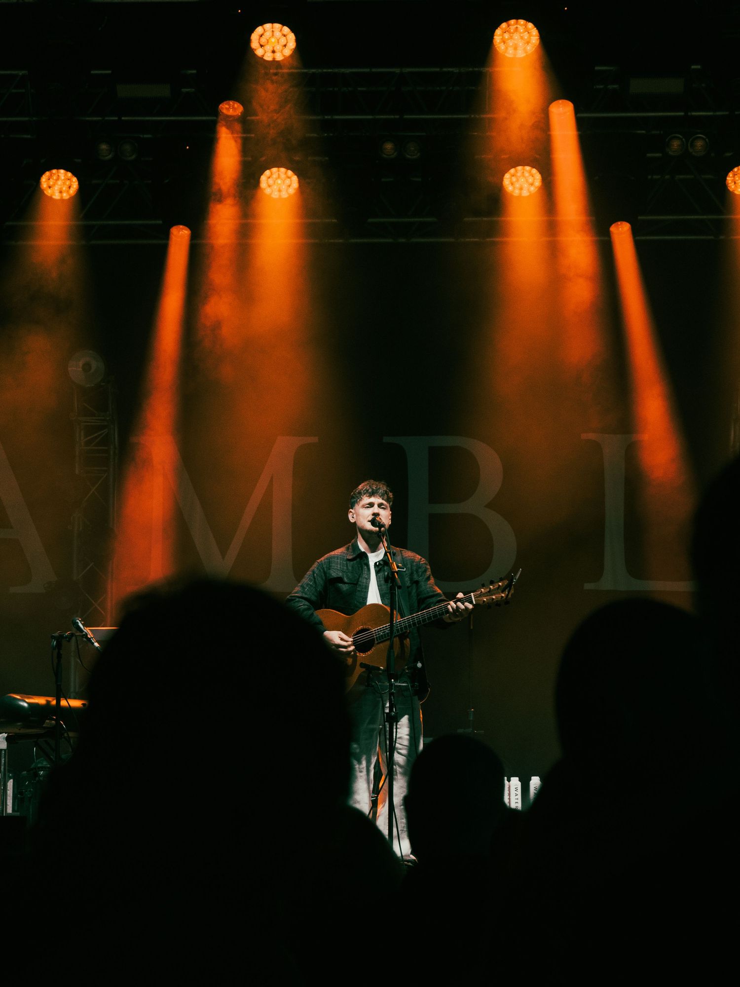 Silhouetted musician performs on stage with dramatic orange lighting and fog effects.
