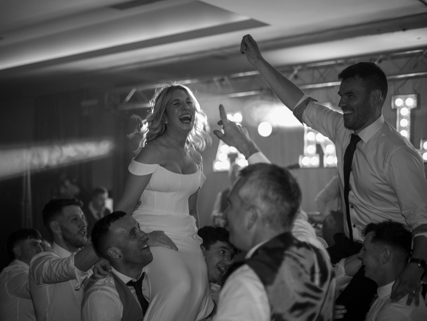 Wedding guests dancing and celebrating on a dimly lit dance floor at a reception party.