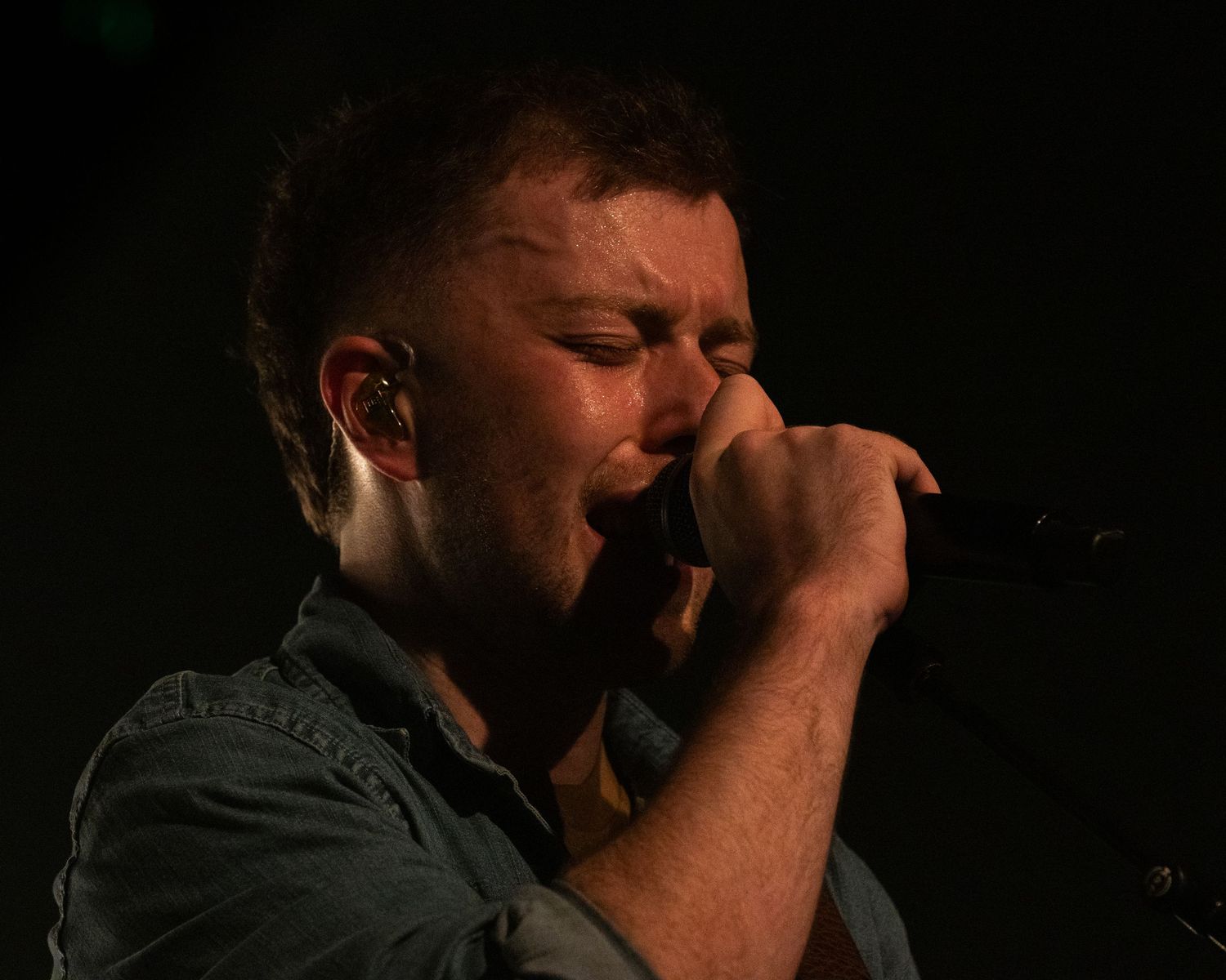 Concert performer singing passionately on stage with dramatic lighting and dark background.