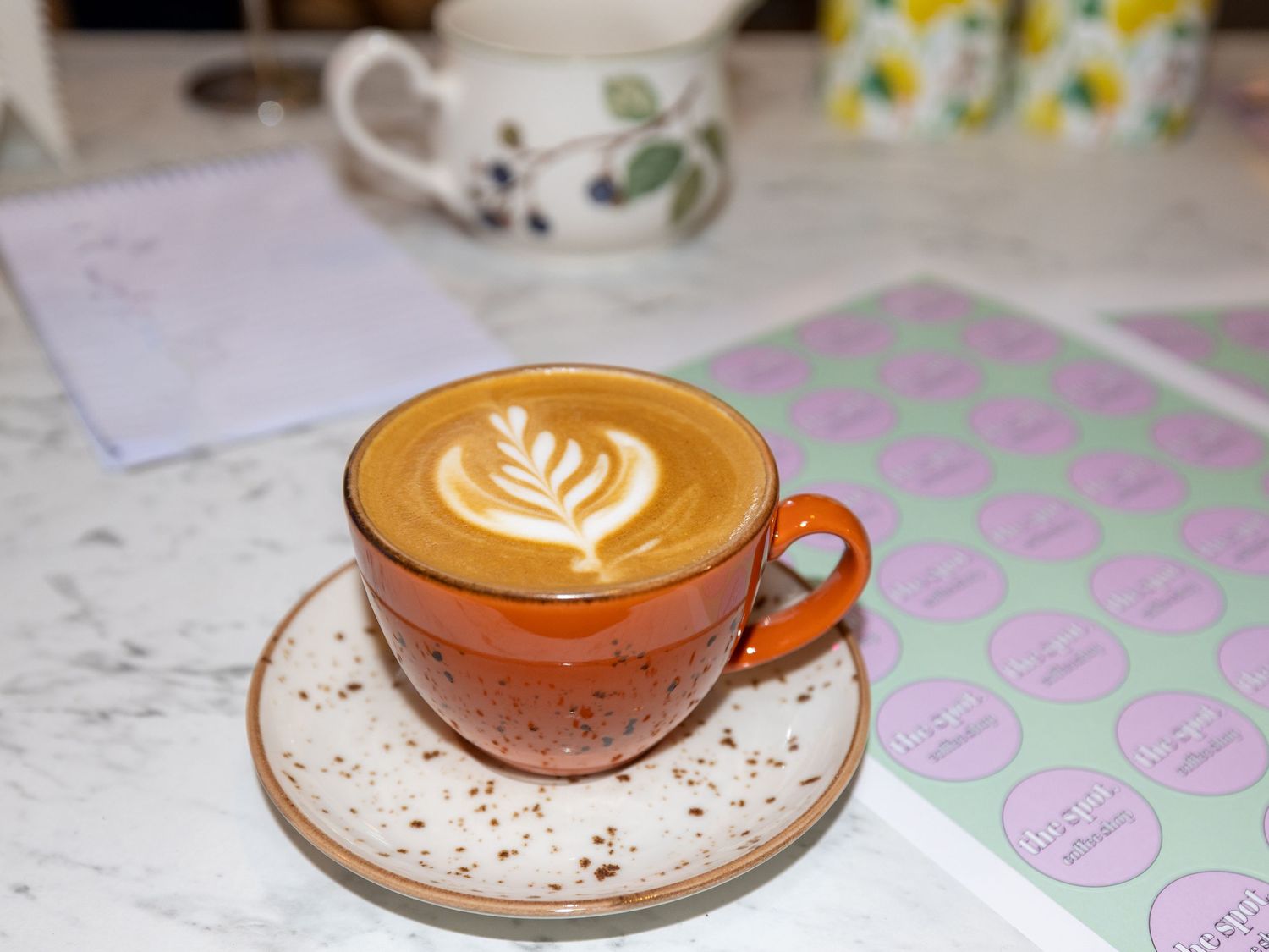 Artfully crafted latte with tulip design foam art served in brown ceramic cup on speckled saucer.