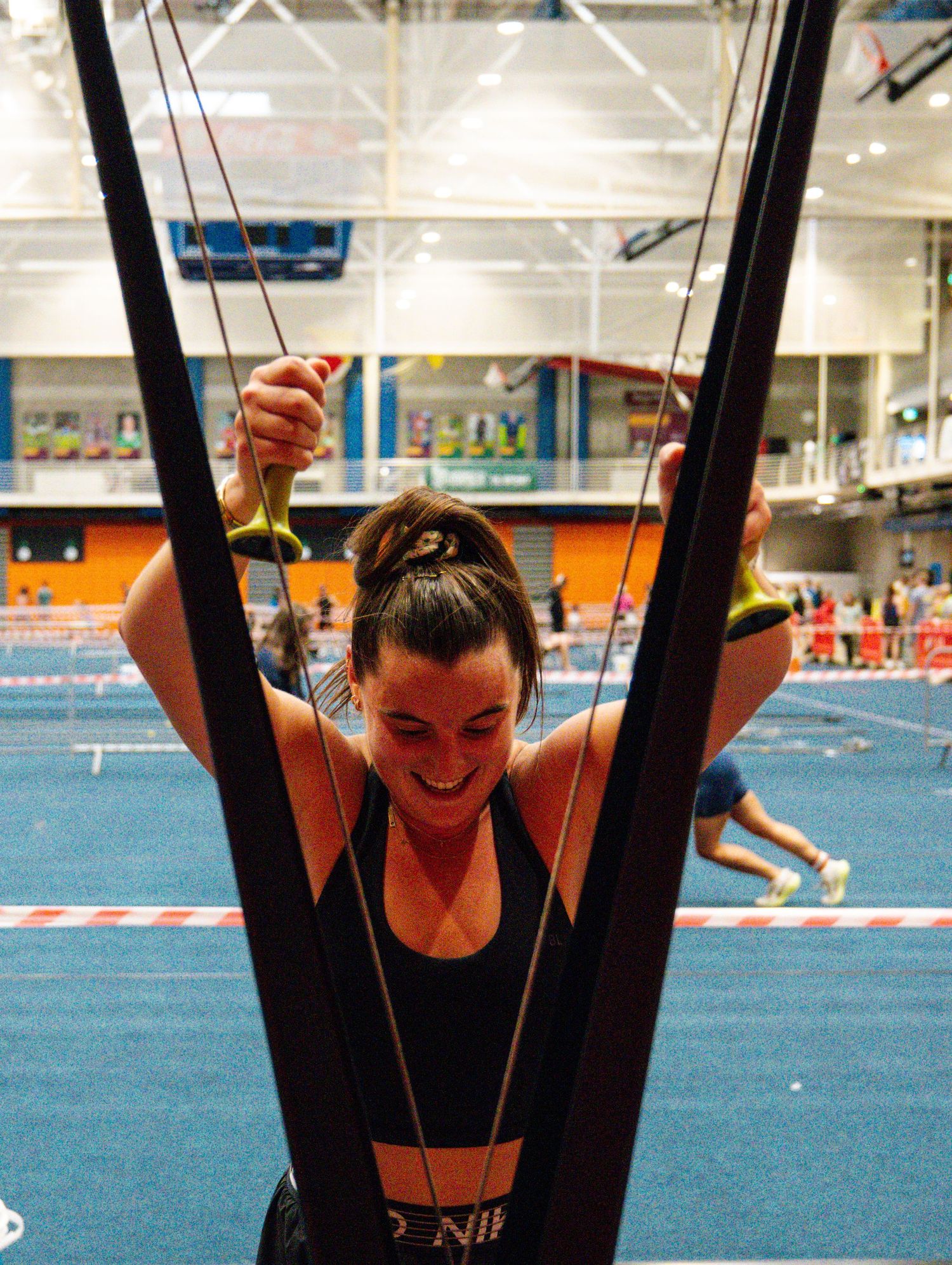 Gymnast performing a sequence of movements on uneven bars in a gymnasium with blue floor mats.