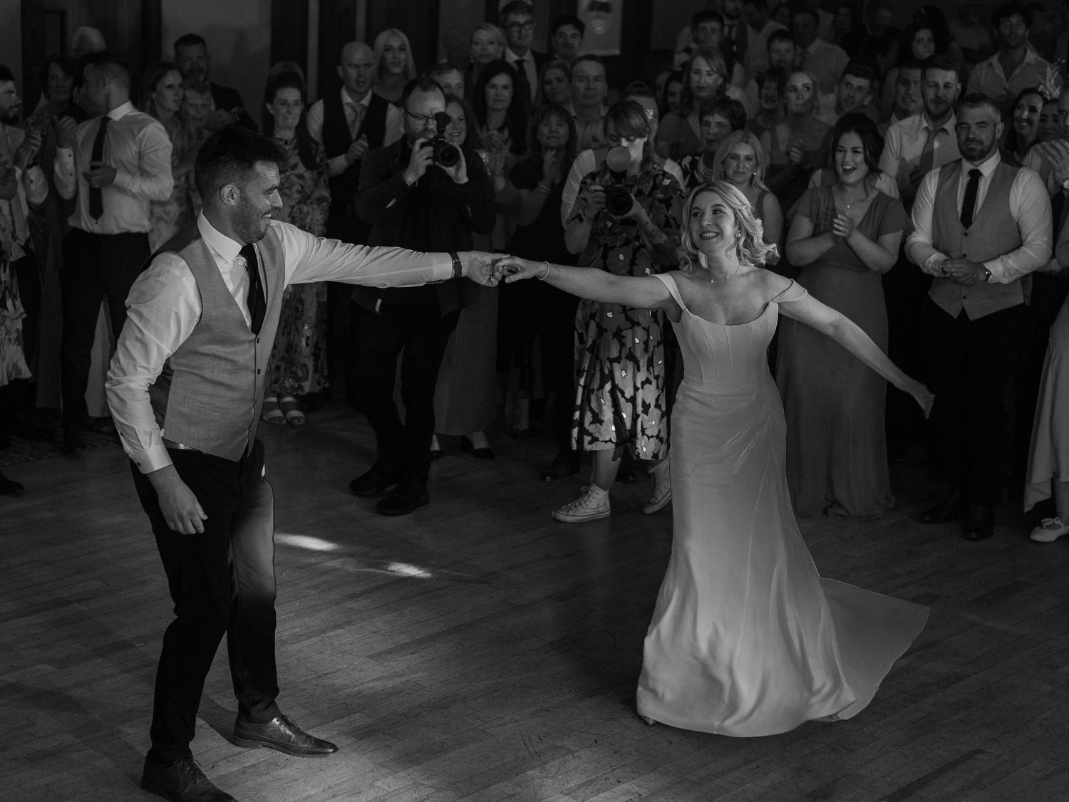 Wedding reception dance floor illuminated with dramatic lighting as guests watch from the sides.