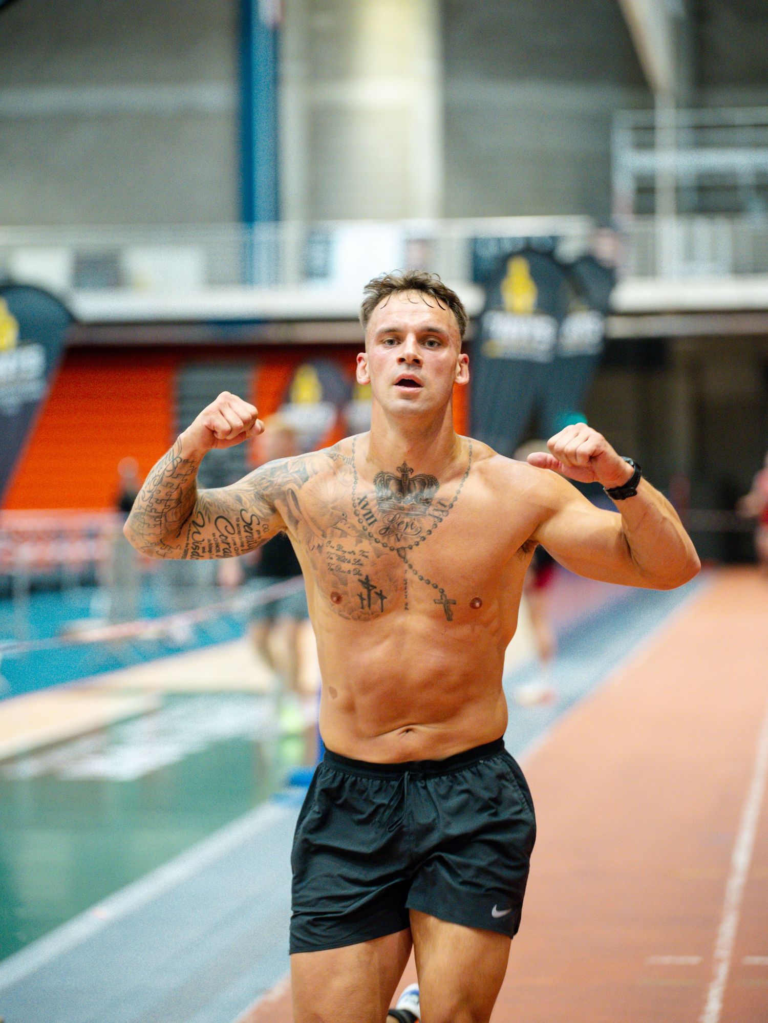 Athletic person in black shorts performs dynamic stretching exercises on indoor running track.