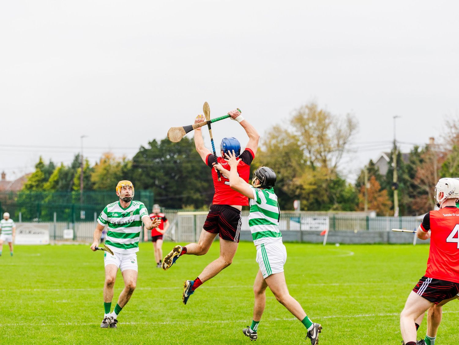 Soccer players in green and white striped jerseys compete against players in red jerseys on a grass field.