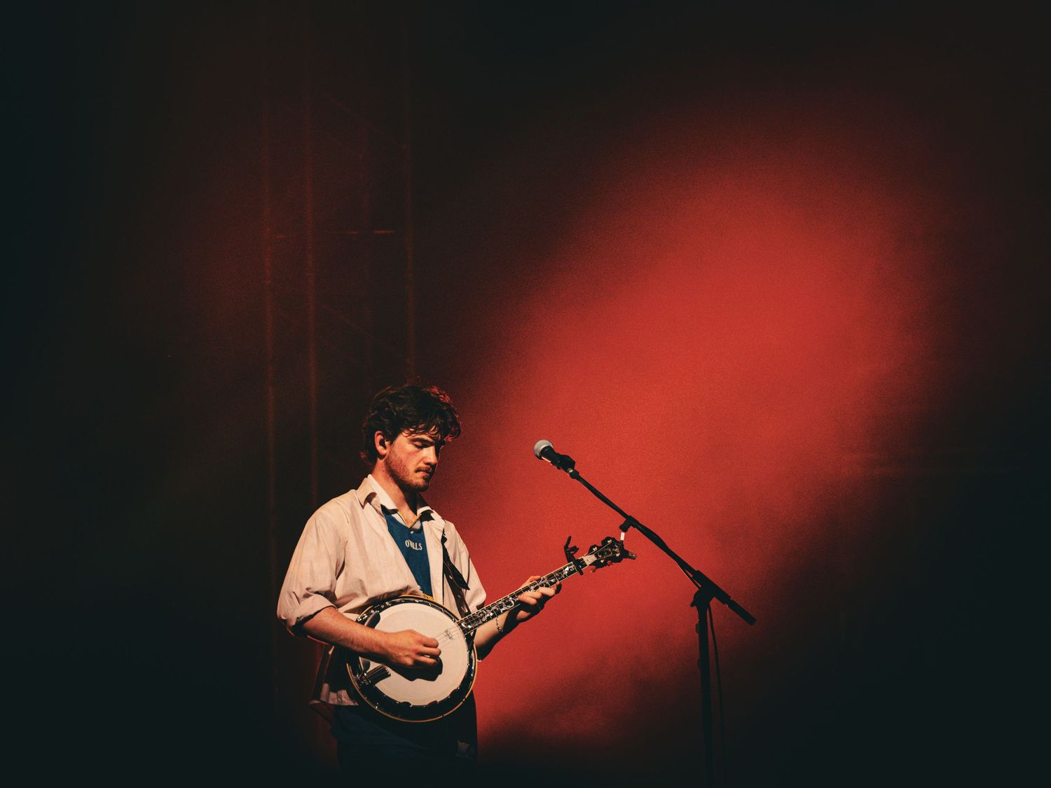 A performer plays banjo on stage with dramatic red lighting and fog effects in the background.