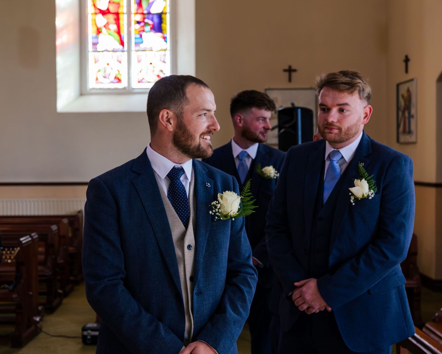 Groomsmen share a lighthearted moment in navy suits inside a church setting.