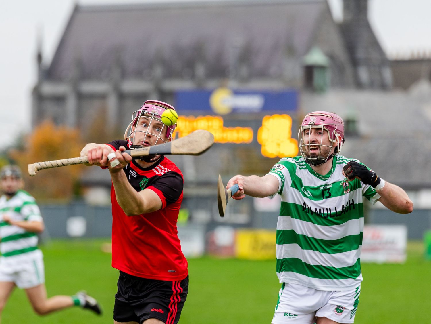Hurling players in red and green striped jerseys compete for possession during an intense match.