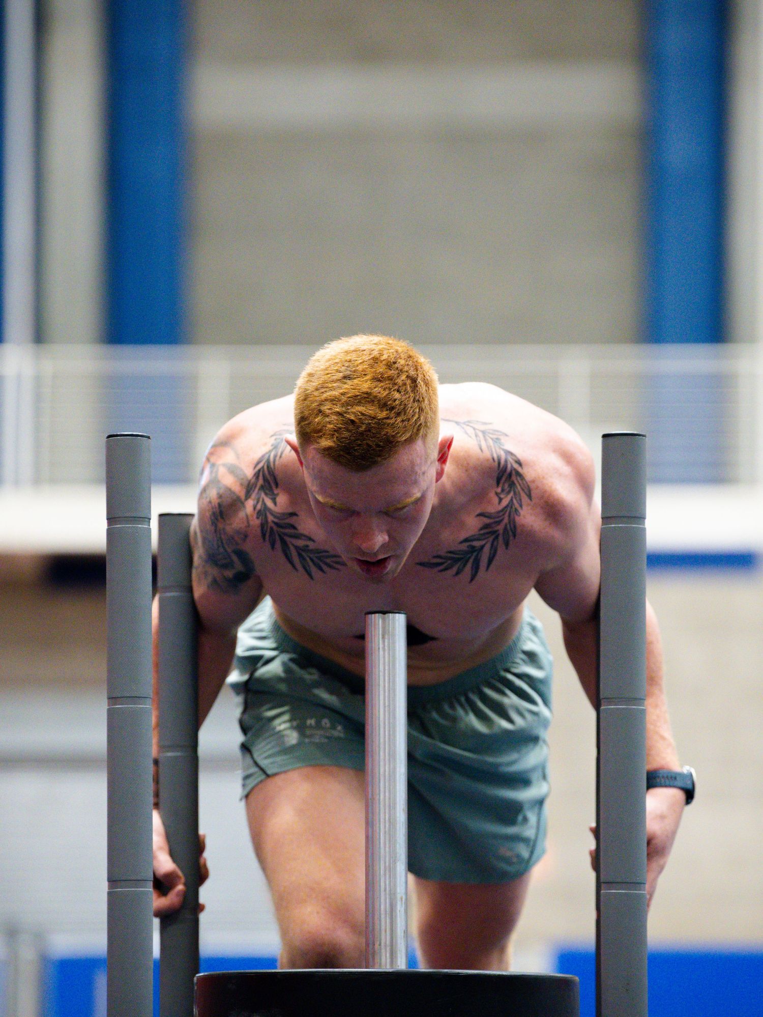 A shirtless athlete performs a rigorous dip exercise on parallel bars during an intense workout session.