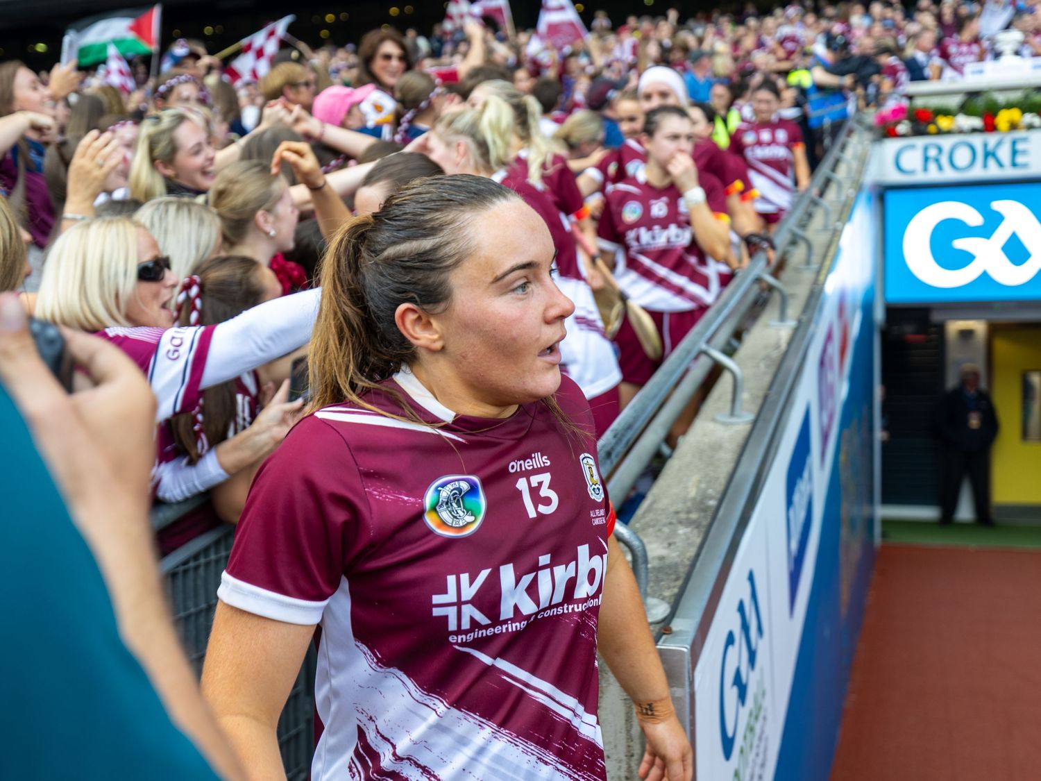 Cheering crowd wearing maroon team colors waves flags and banners at a sporting event.