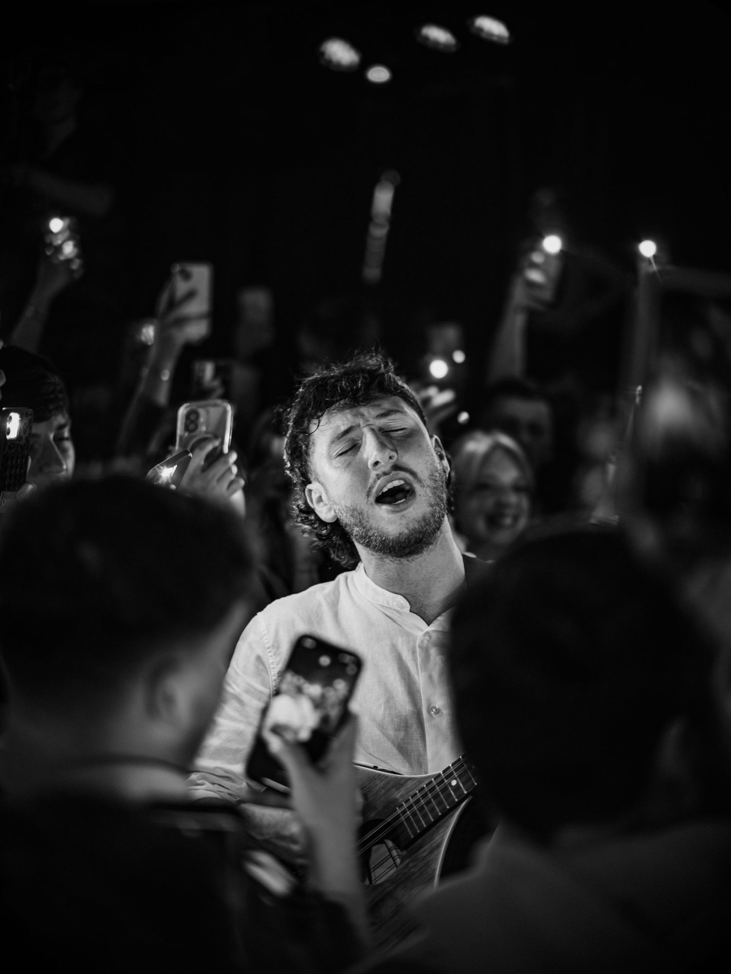Concert crowd silhouettes with raised phones capturing a passionate performance moment.