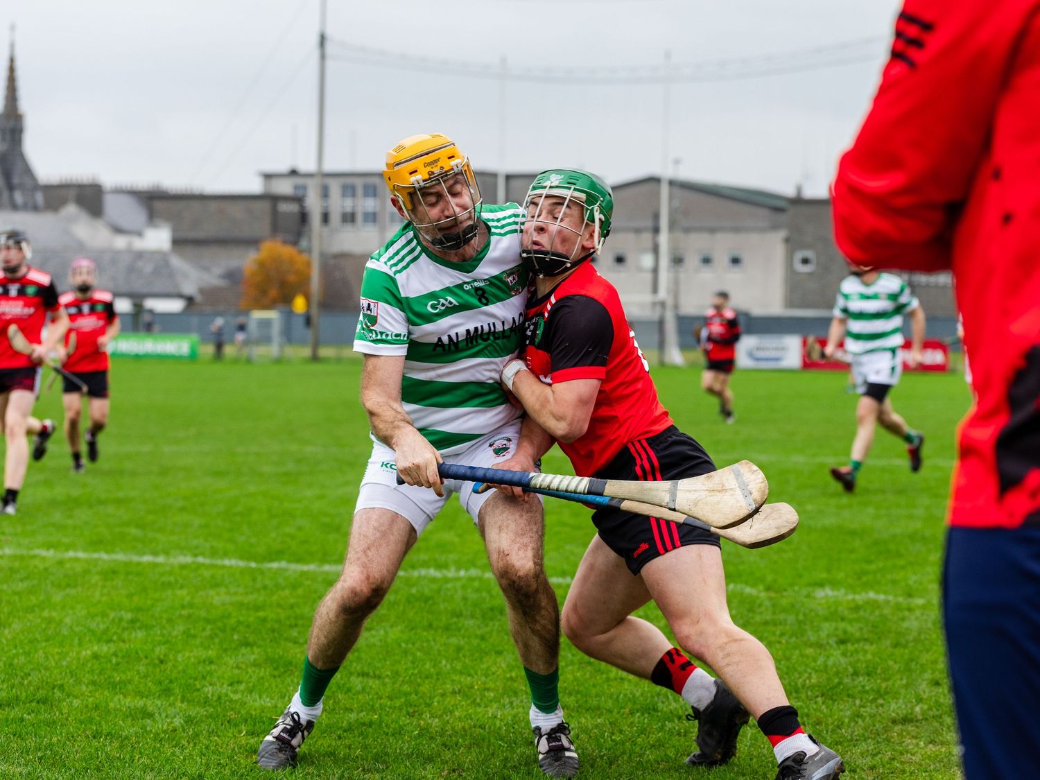 Rugby players in green and red jerseys compete for possession during a match on a grass field.