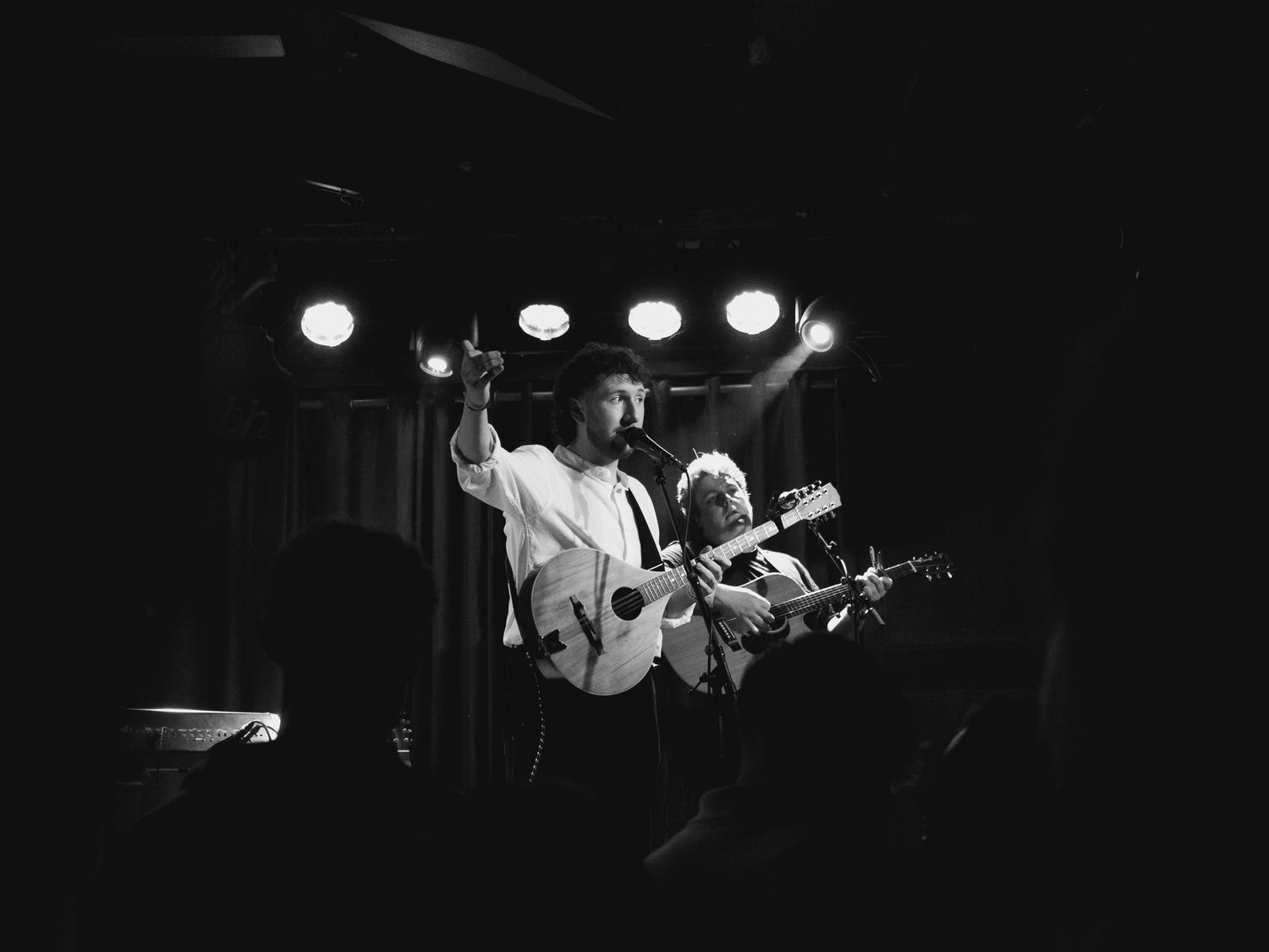 Band performs on dimly lit stage with spotlights and silhouetted musicians.
