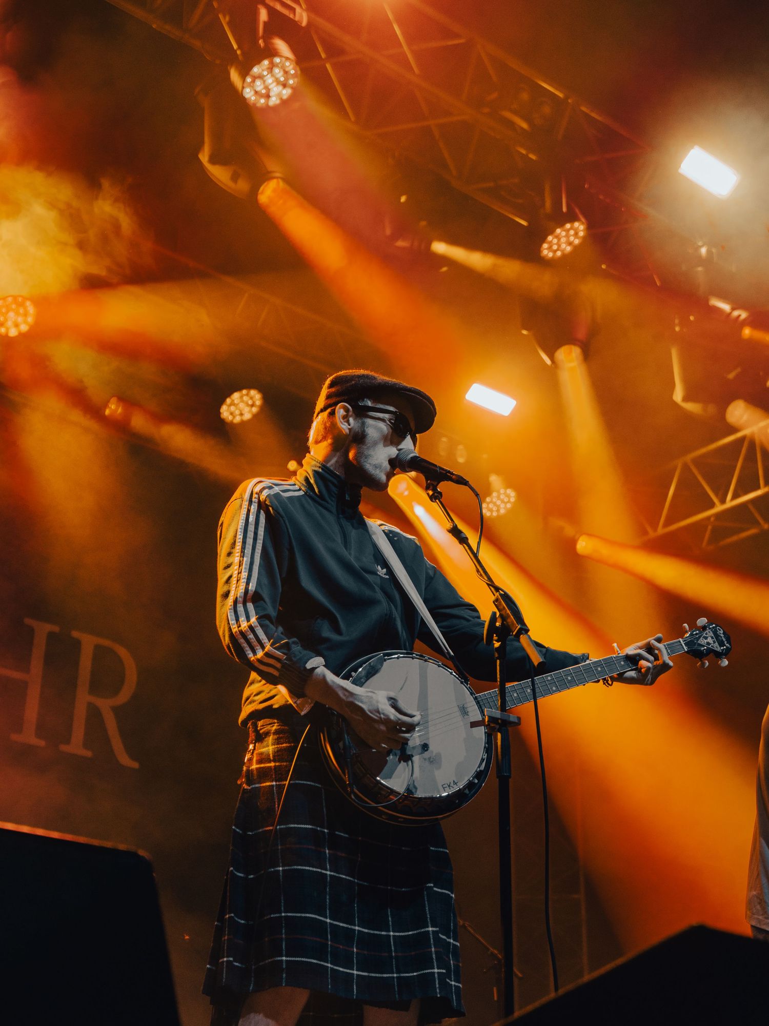 A performer plays guitar on stage bathed in warm orange lighting with theatrical spotlights overhead.