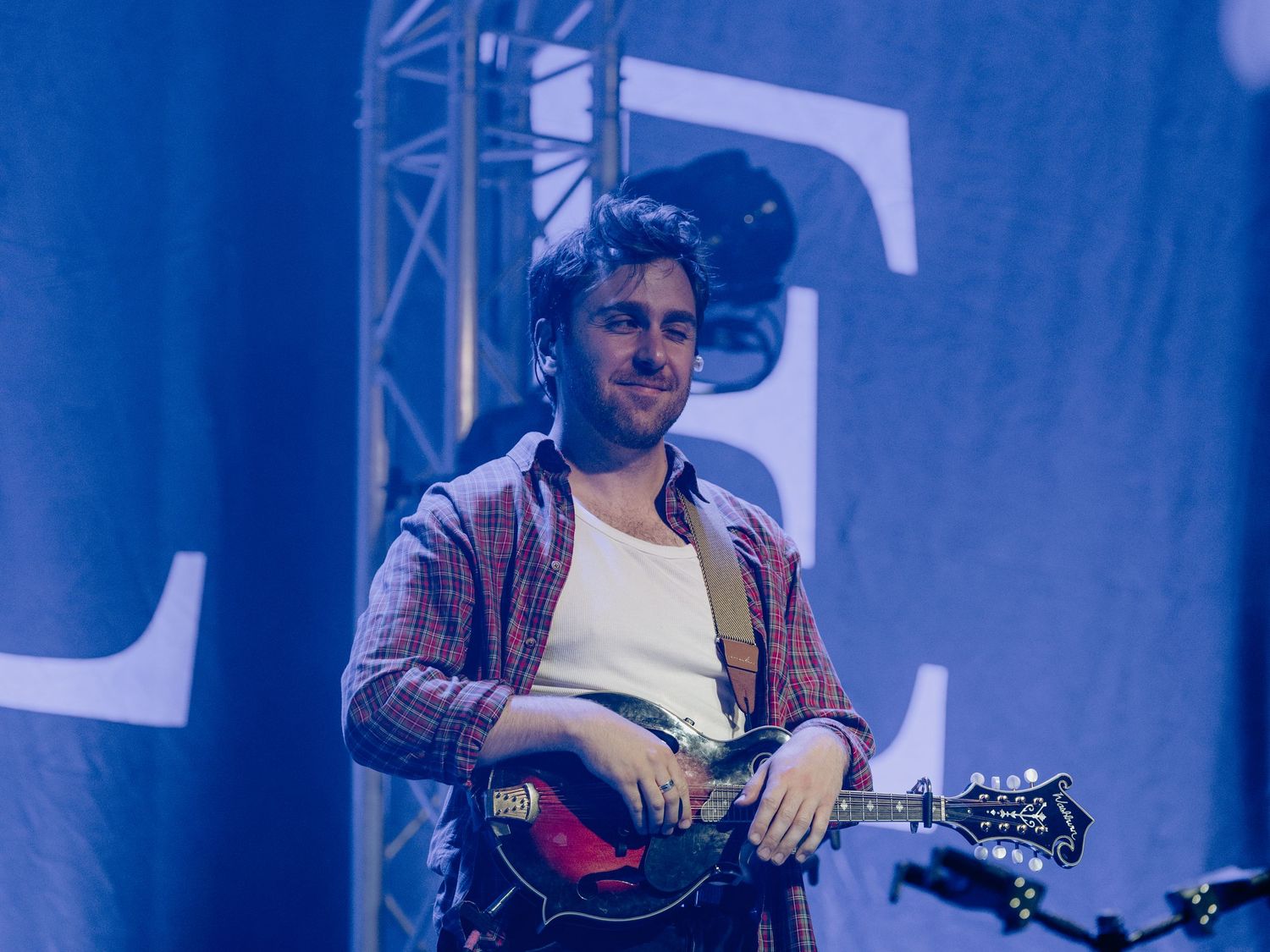 Musicians perform on brightly lit blue stage with professional lighting and equipment.