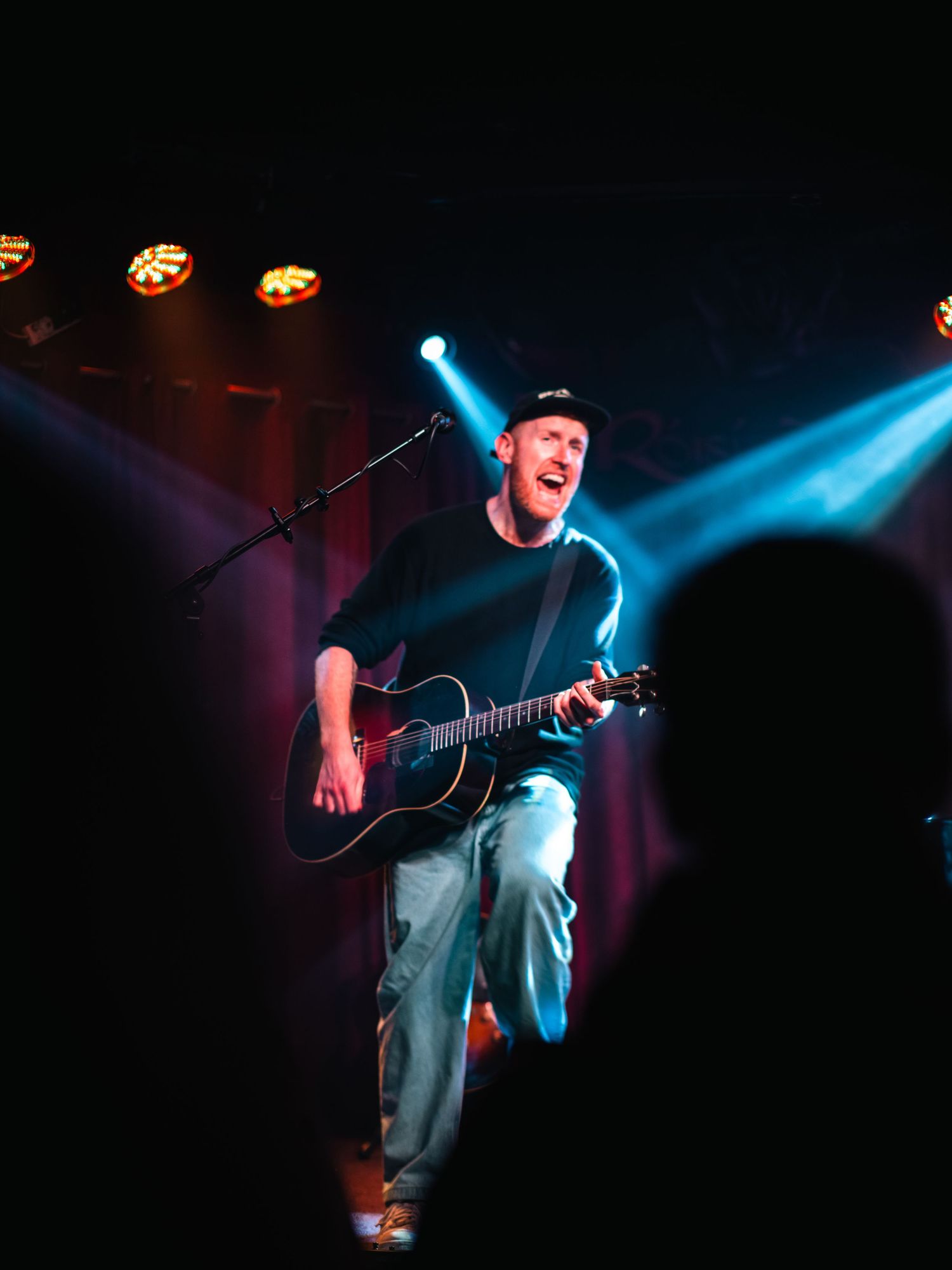 Musician performing on stage with bright blue spotlights creating dramatic concert atmosphere.