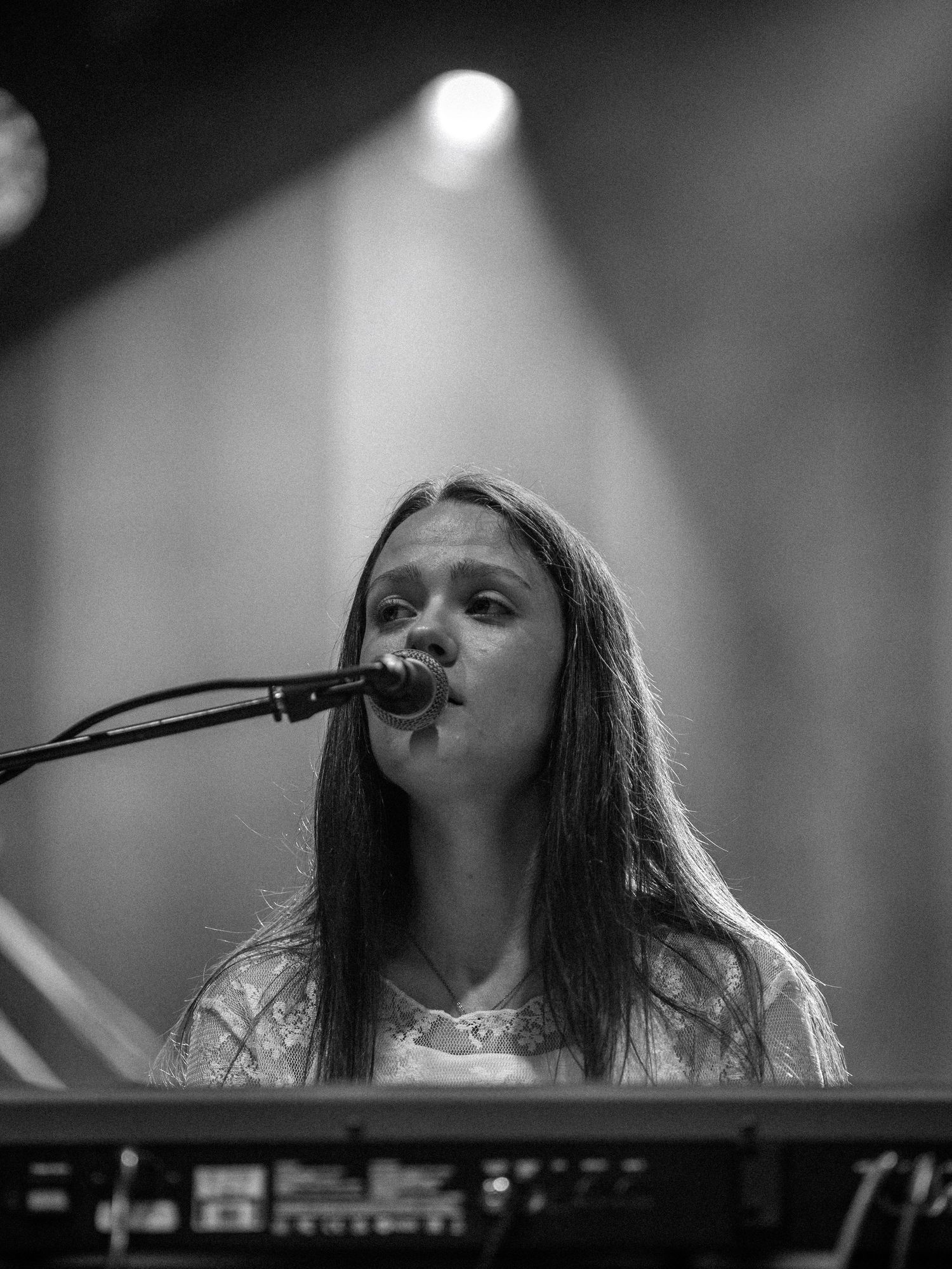 Musician performs at keyboard under dramatic stage lighting in black and white concert photo.