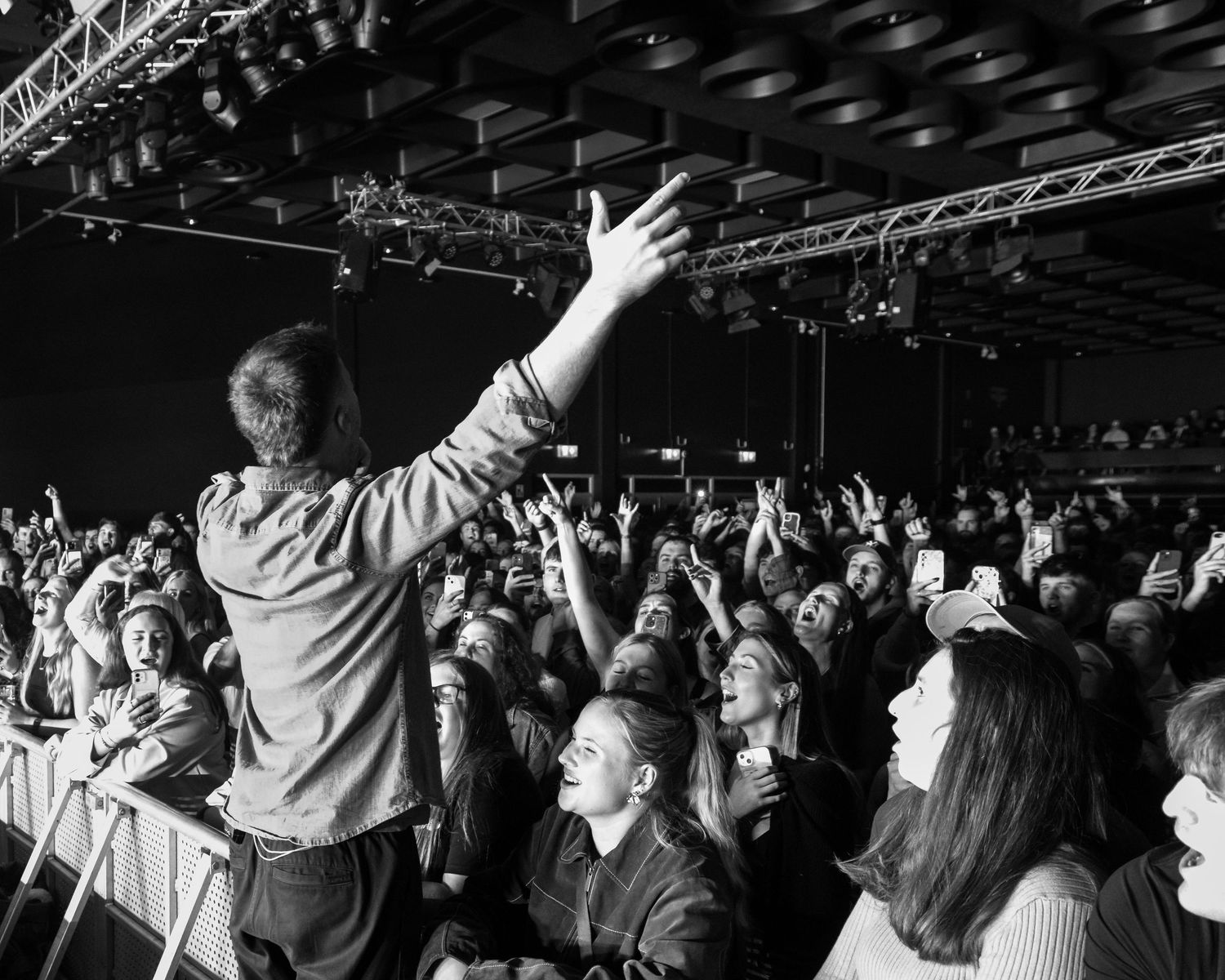 Concert crowd with raised hands enjoying live music performance in black and white photography.