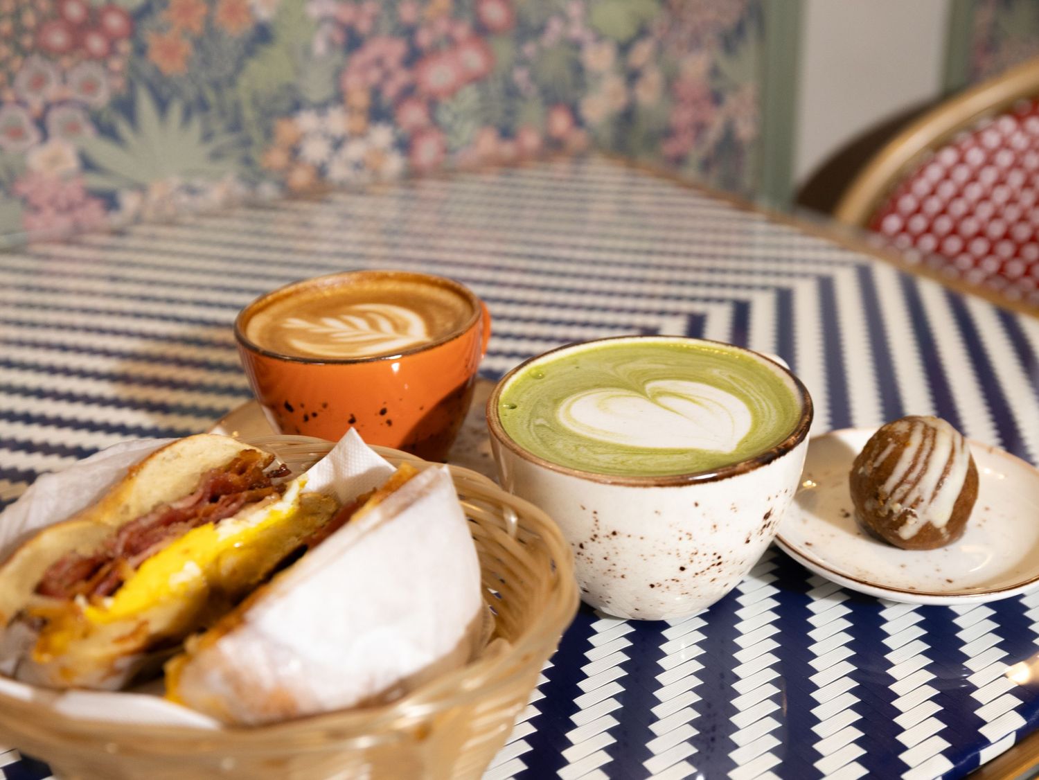 A row of colorful latte art drinks and pastries arranged on a blue and white striped tablecloth.