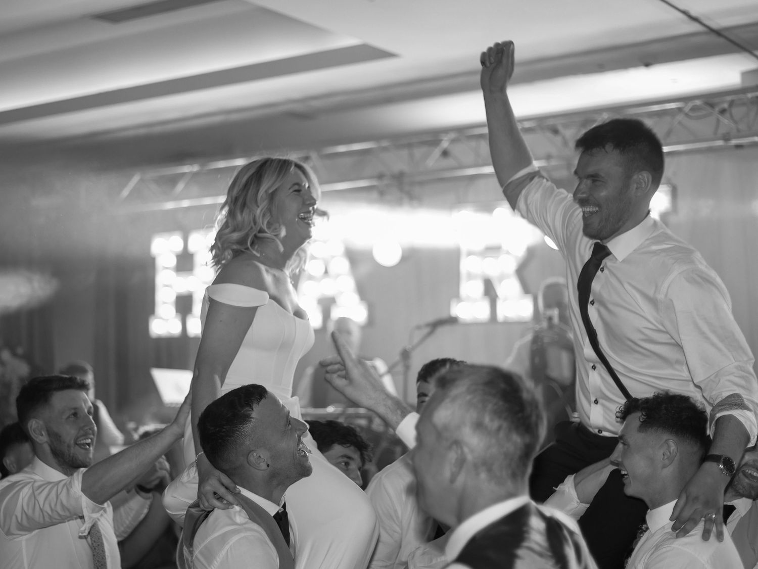 Black and white photo of wedding reception dancing with raised hands.