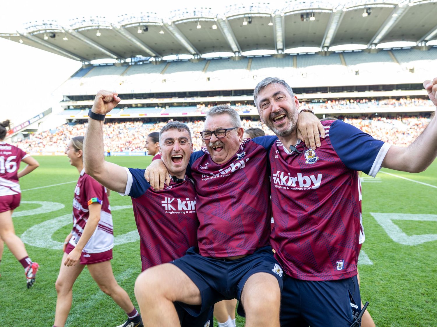 Team players in maroon uniforms celebrating together on a sports field.