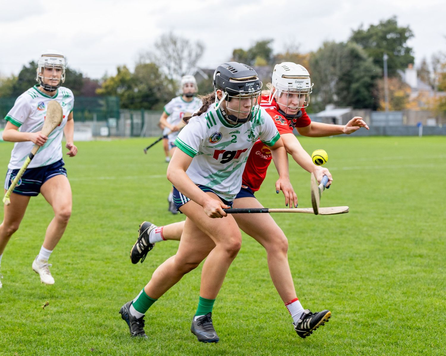 A sequence of four action shots showing a camogie player diving to scoop up a ground ball during a match.