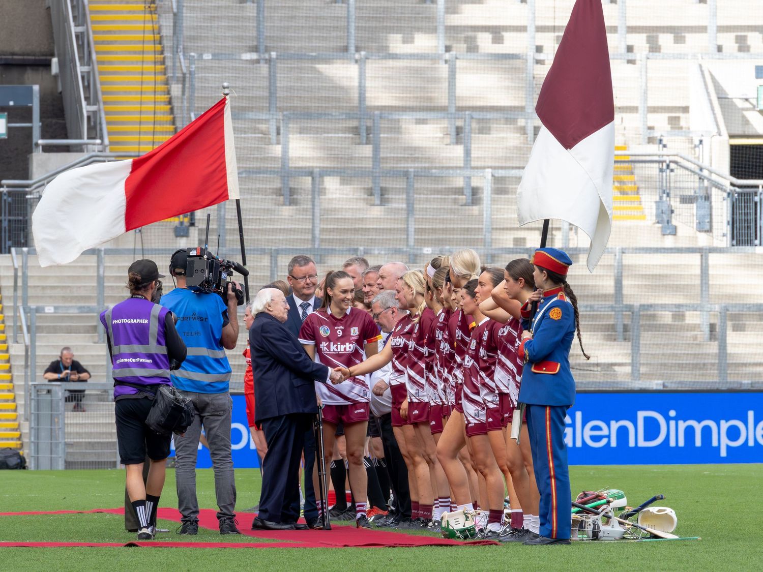 Rugby players huddle together on the field during a match while wearing maroon and white striped jerseys.