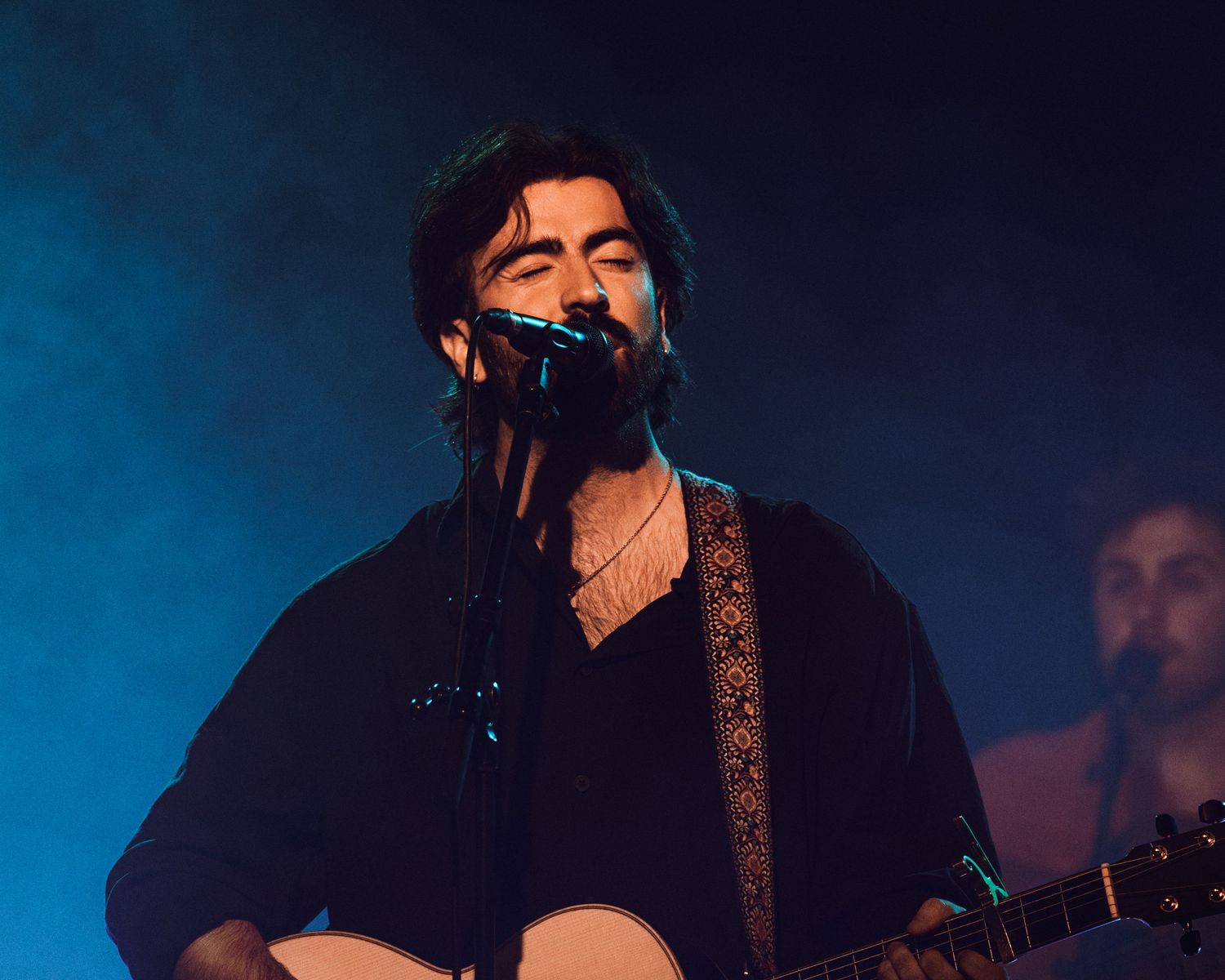 Musician performs on stage with guitar against dramatic blue lighting and fog effects.